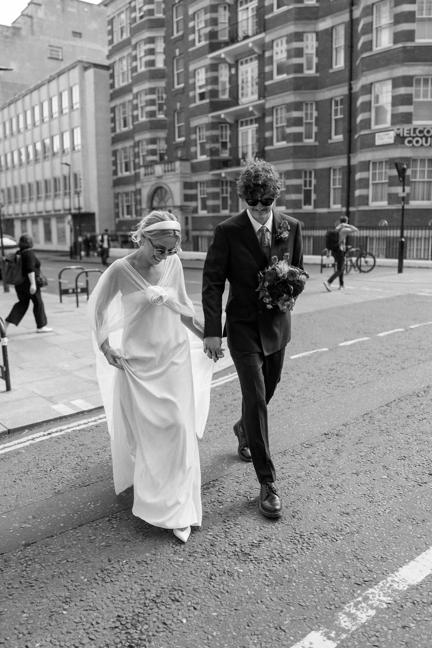 A couple walks along a brick-lined street in front of classic London architecture.