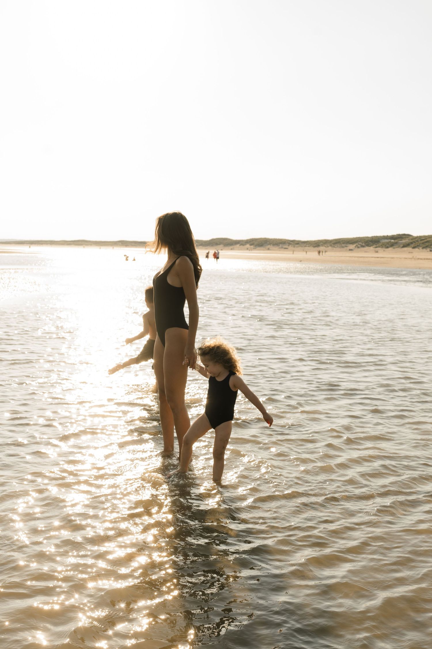 Two people playing in gentle ocean waves during golden hour at the beach.