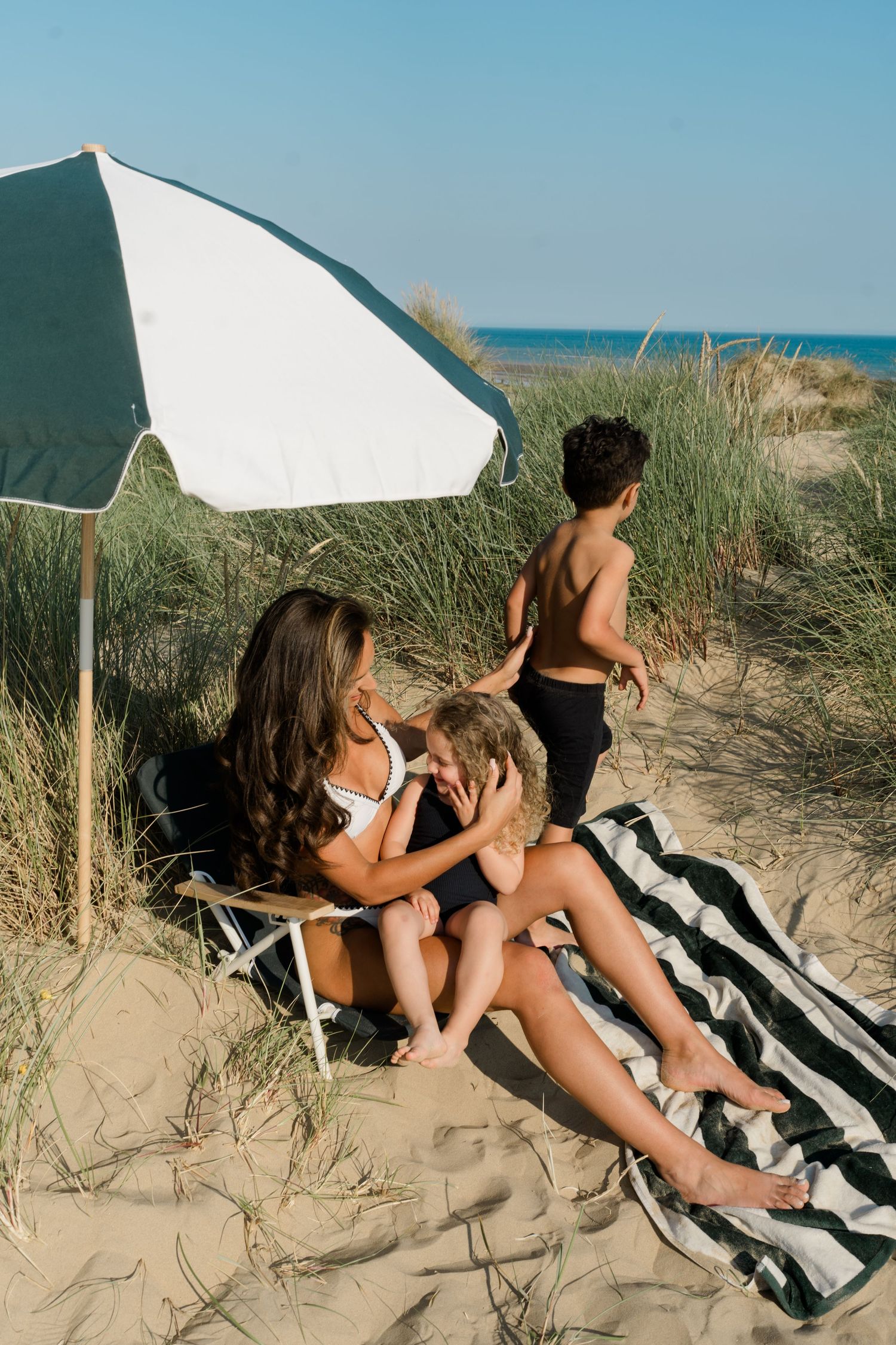 Friends relaxing together on beach blanket under umbrella surrounded by dune grass.