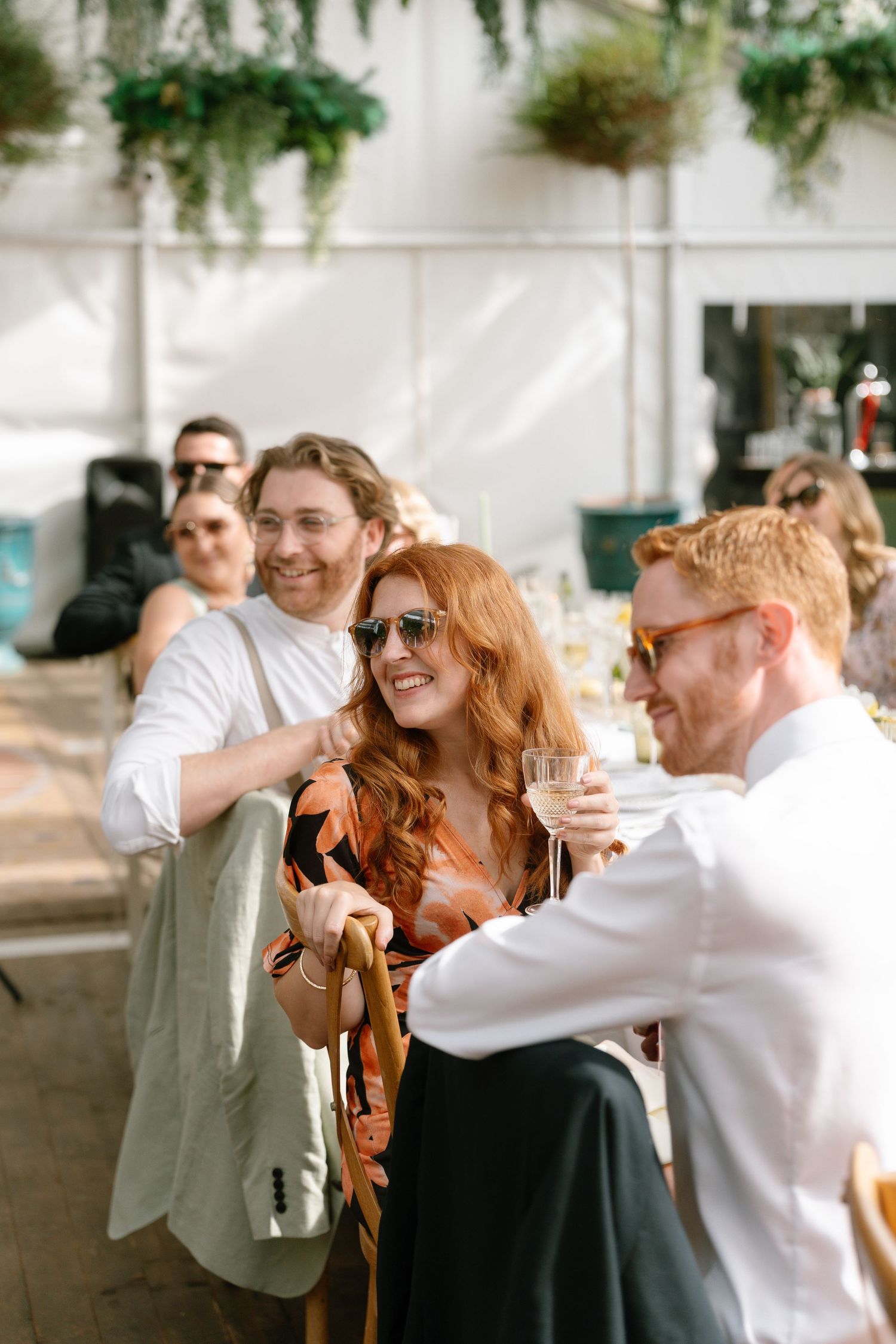Wedding guests enjoying conversation during an outdoor reception under hanging greenery.