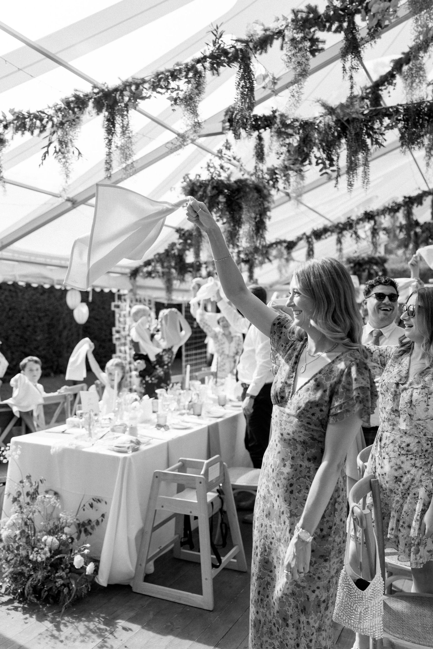 Guest waving napkin during celebration under tent with hanging greenery decorations.