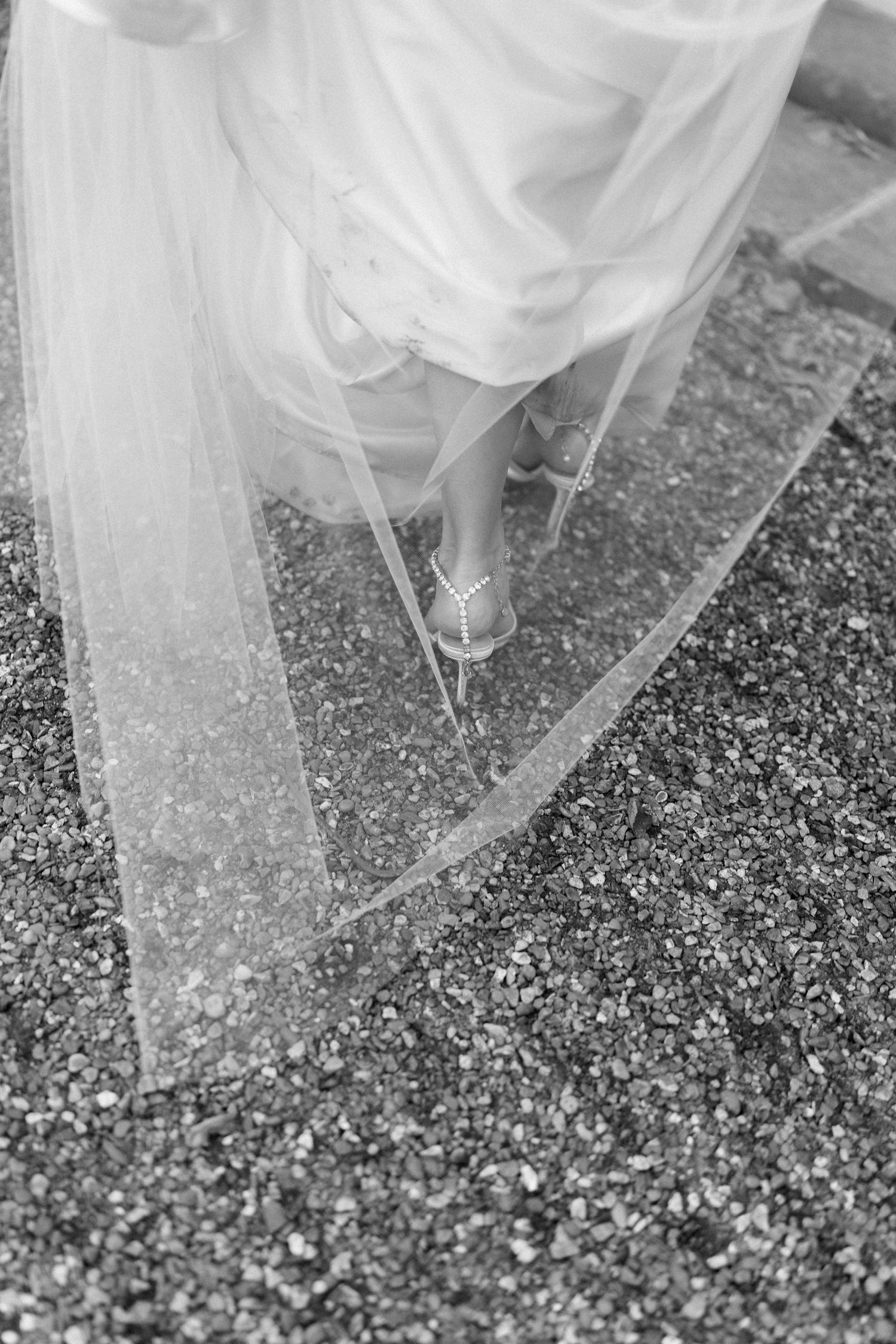 Close-up detail of white wedding dress and confetti on gravel ground.