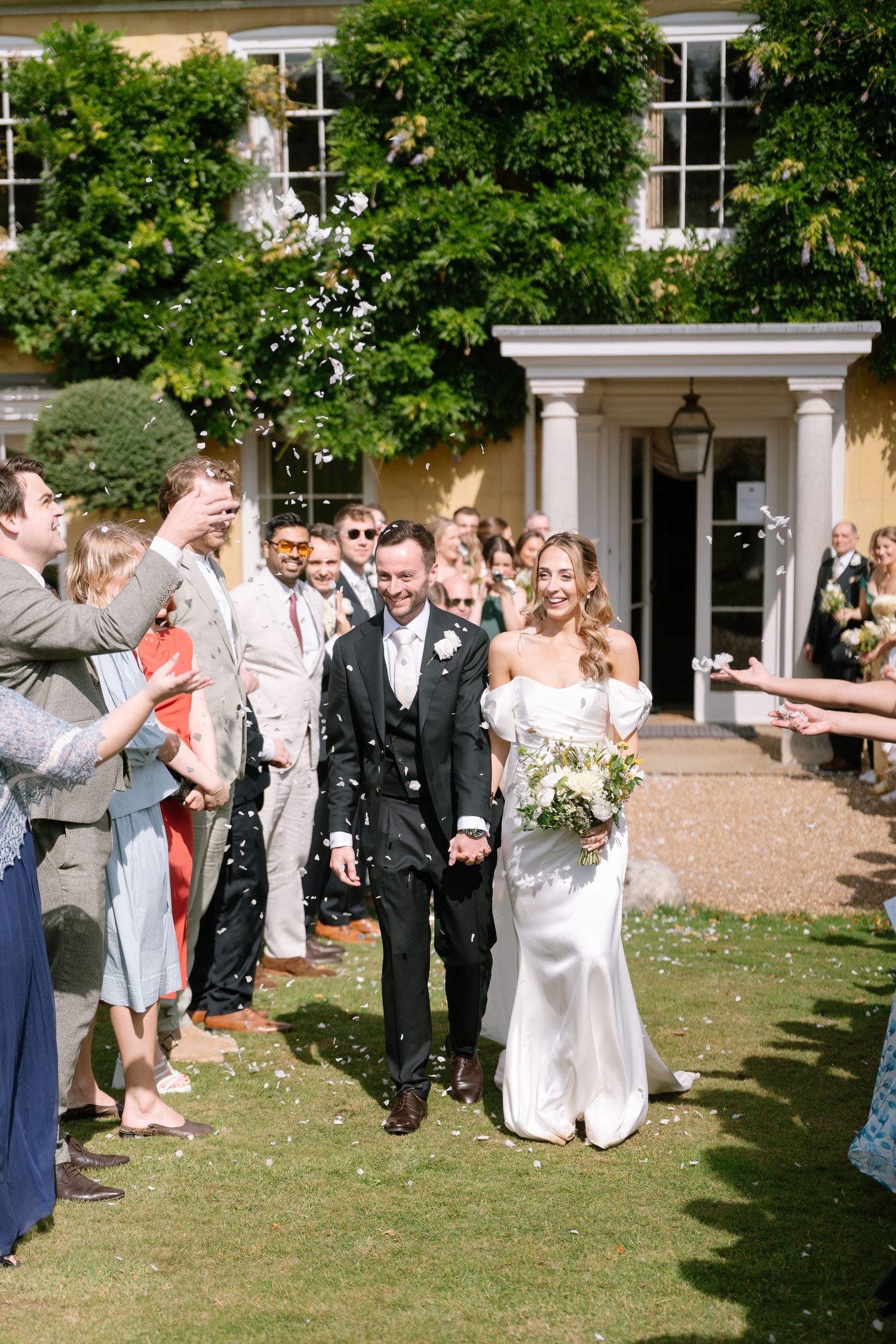 Wedding party processes across the lawn while guests celebrate with confetti.
