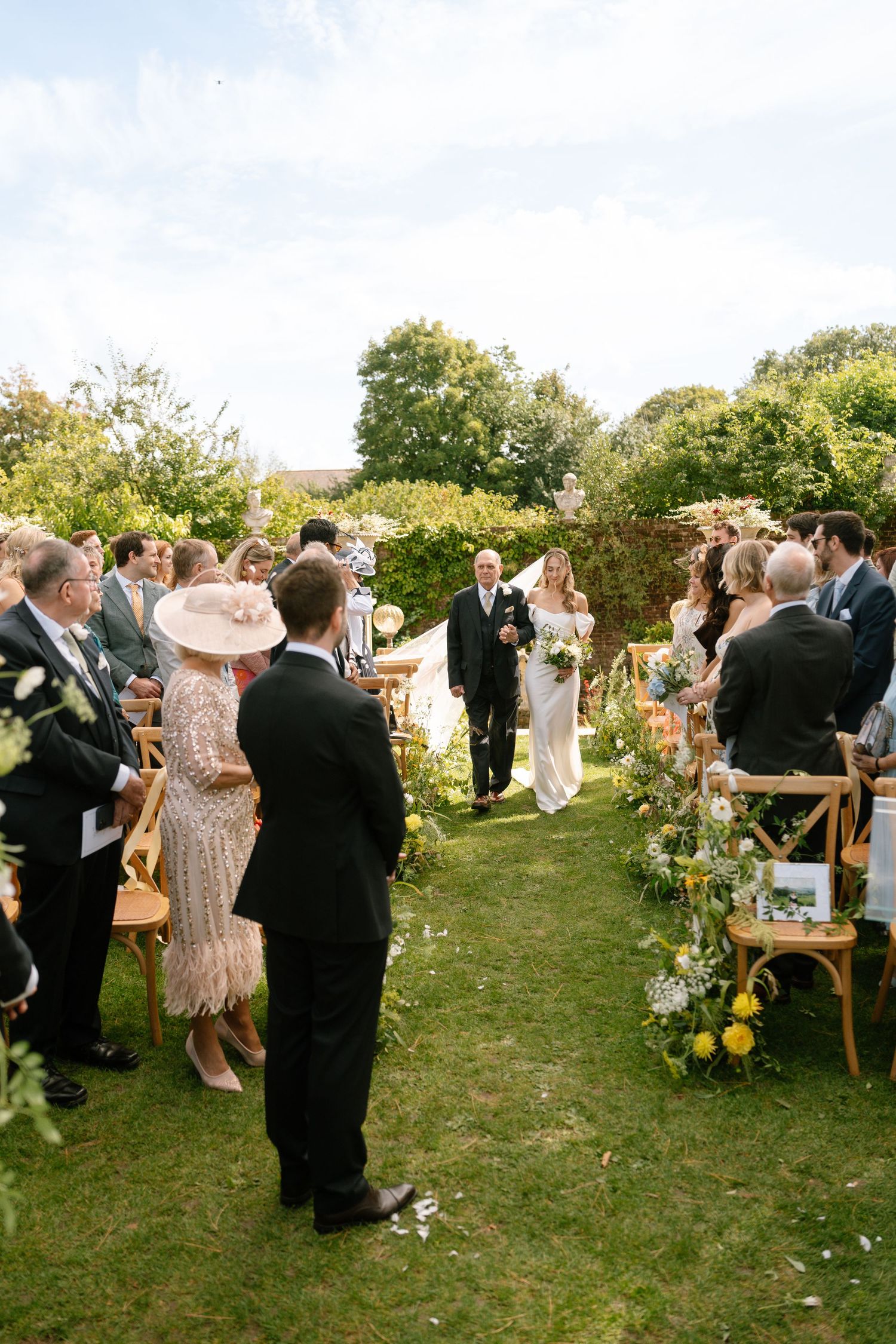 Elegant outdoor wedding reception with guests mingling on a grassy lawn surrounded by greenery.