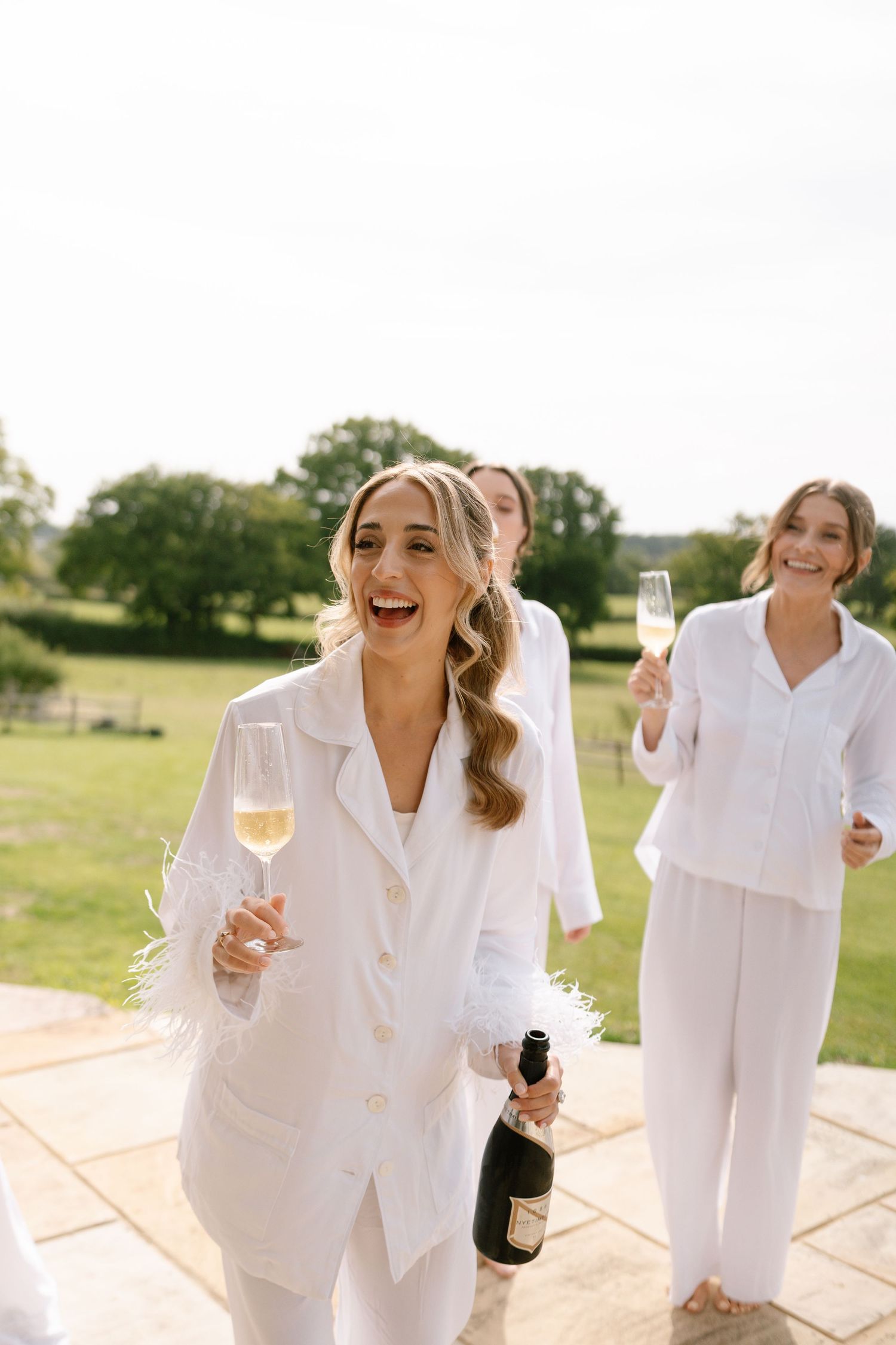 People in white suits celebrate with champagne on an outdoor patio during a sunny day.