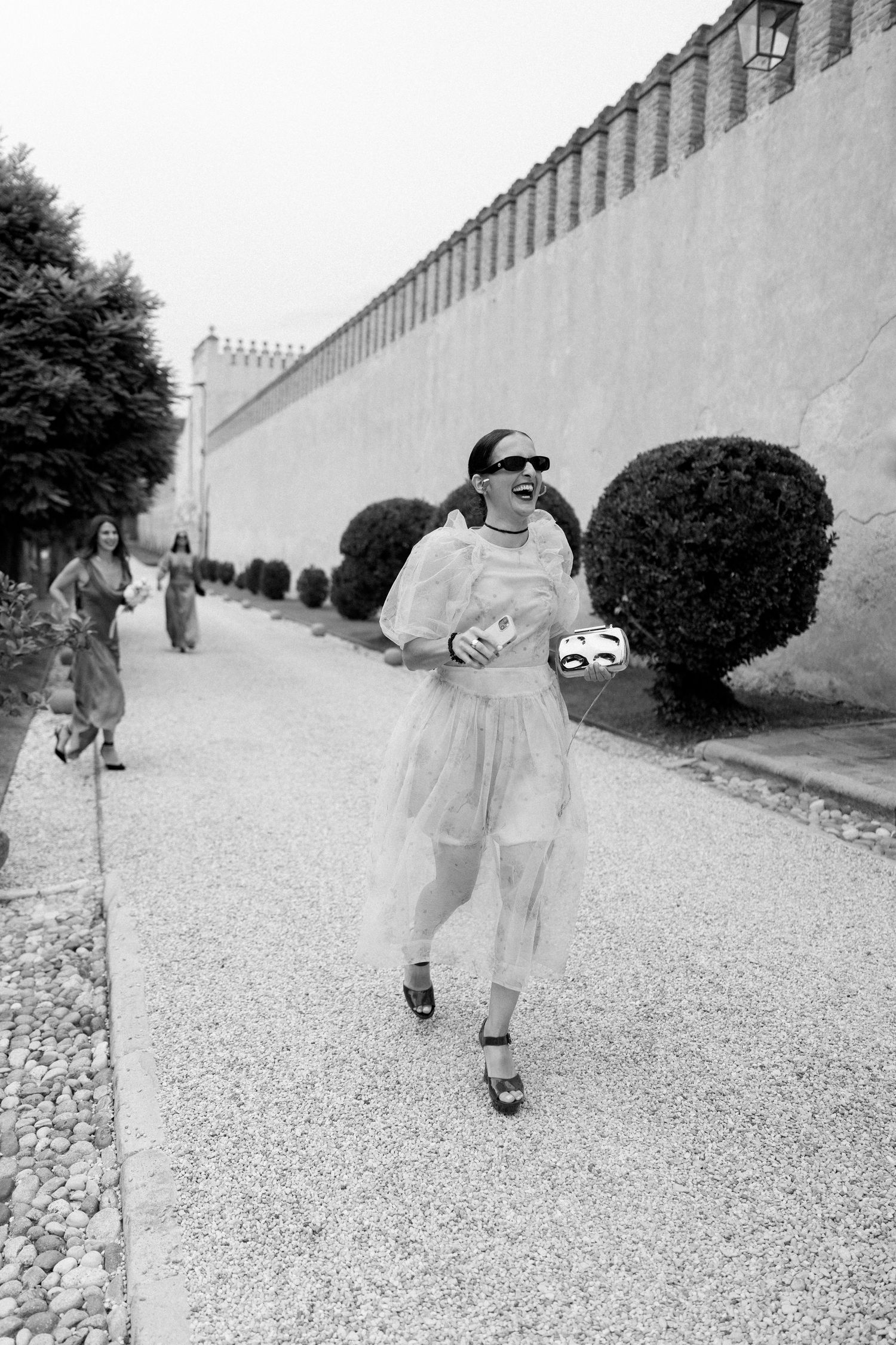 People walking along a gravel path beside a long white stone wall.