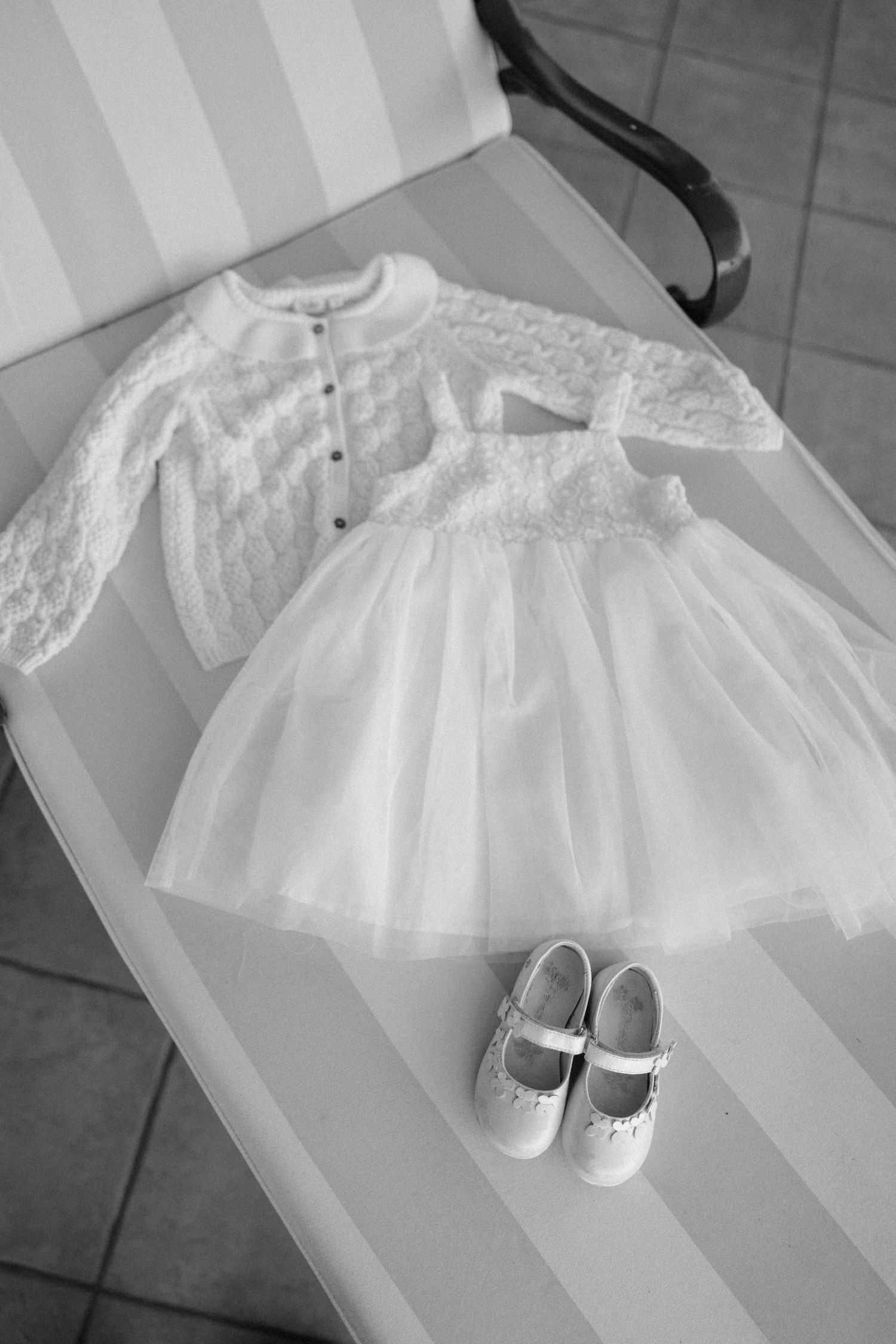 White lace christening gown with matching shoes laid flat on grey surface.