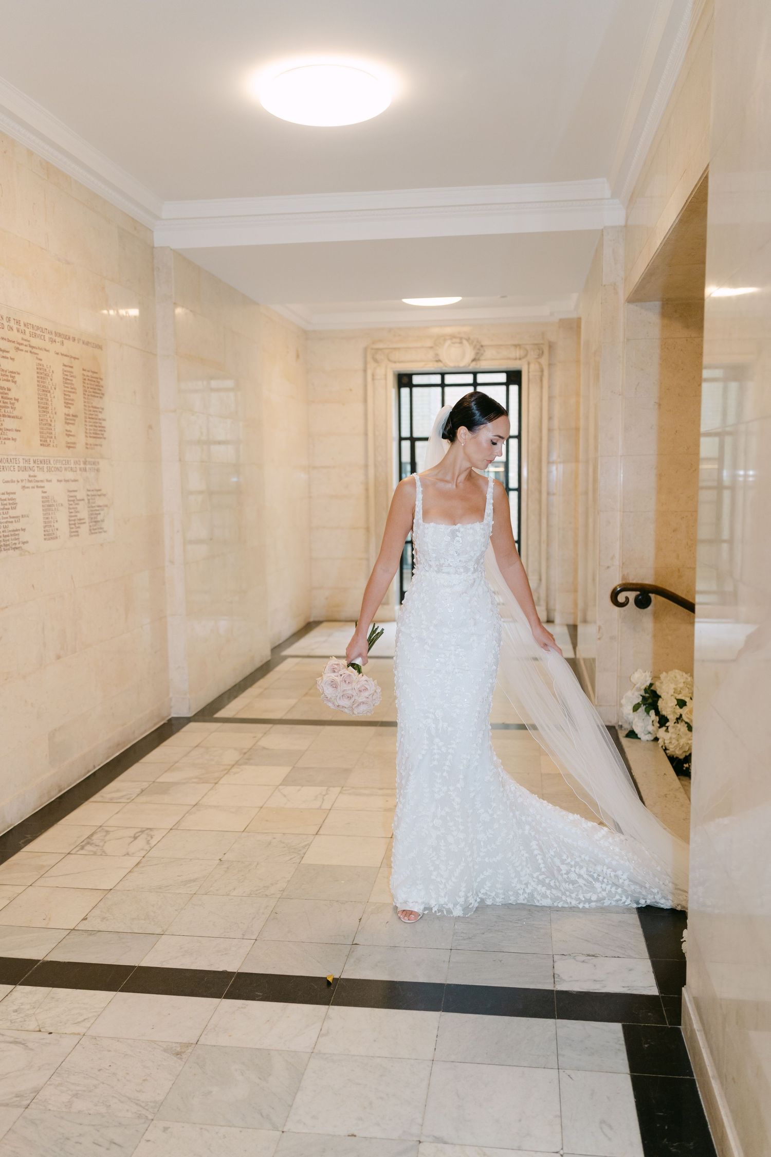 A bride walks through an elegant marble hallway in a fitted lace wedding gown.