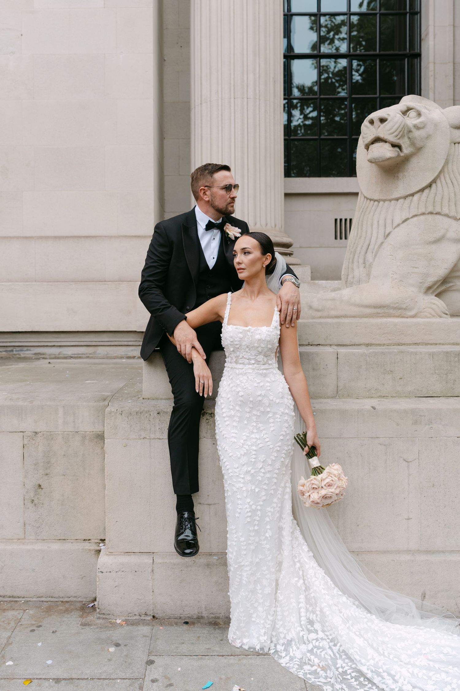 Newlyweds pose elegantly against white stone columns in classic wedding attire.