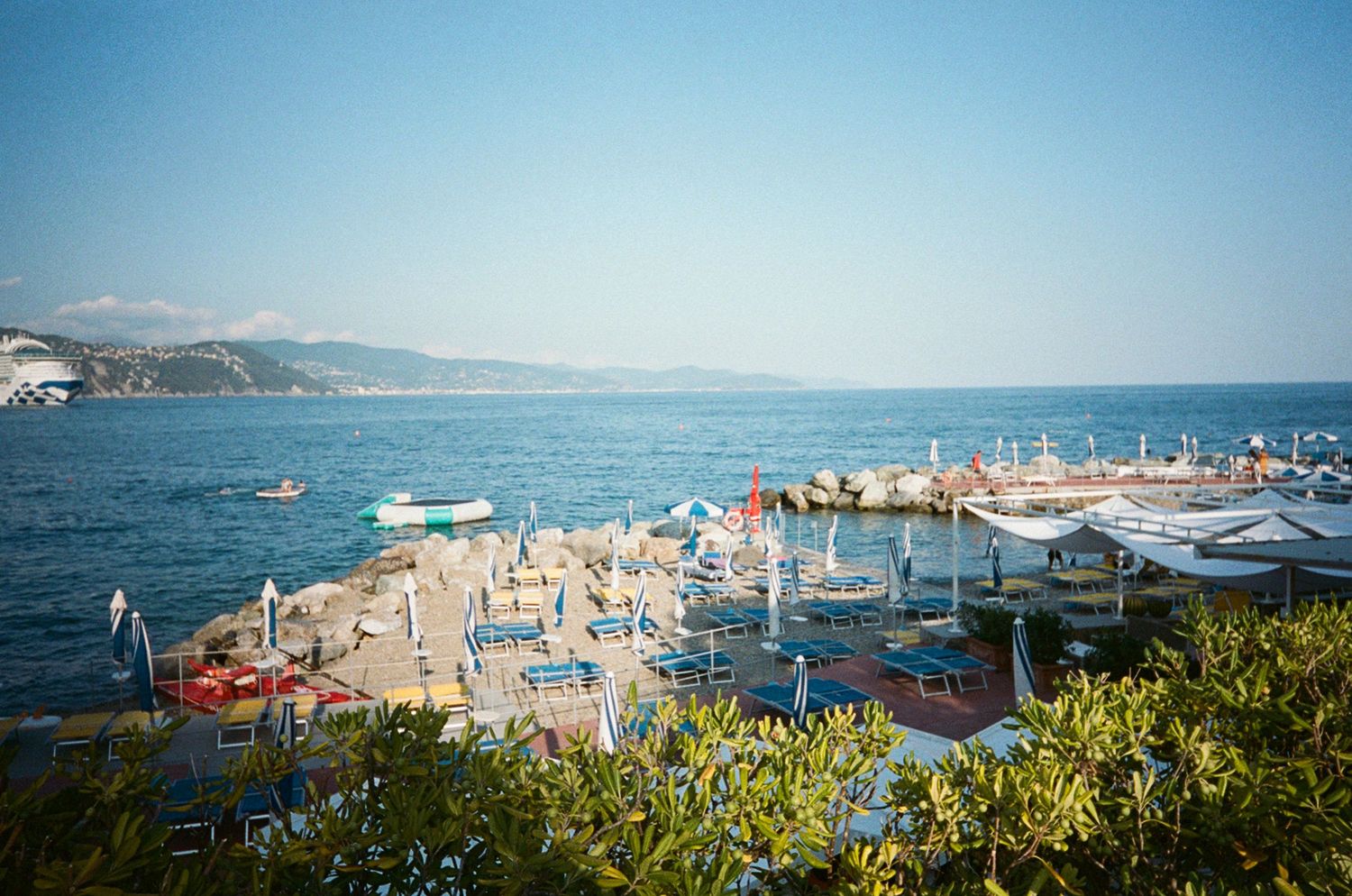 Aerial view of a crowded Italian beach resort with colorful umbrellas, calm blue sea, and scenic coastal hills in summer.