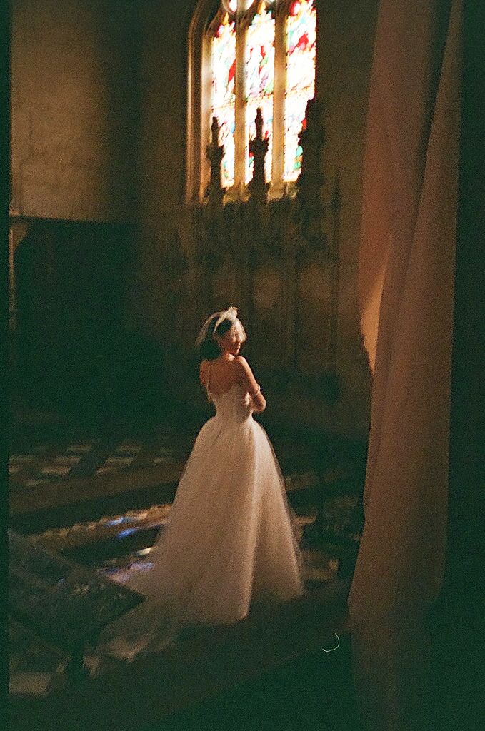 Ethereal silhouettes of bride in ballgown captured in dark church interior with illuminated stained glass windows.