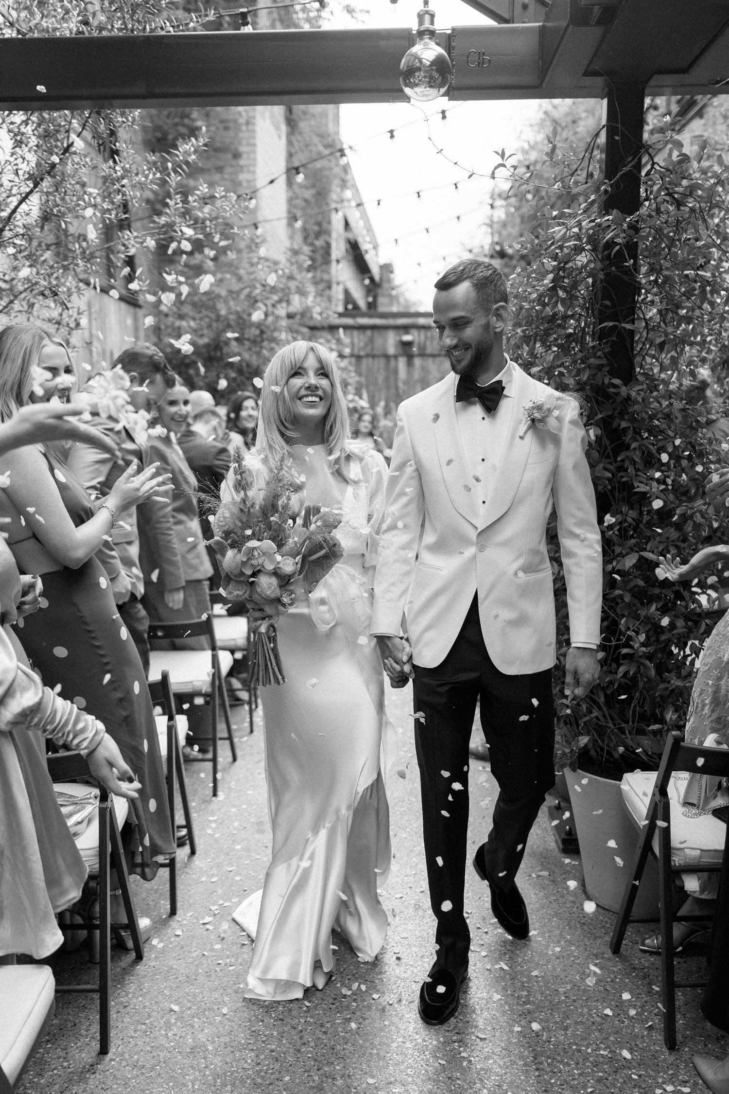 Wedding celebration with guests throwing confetti in a joyful outdoor procession.