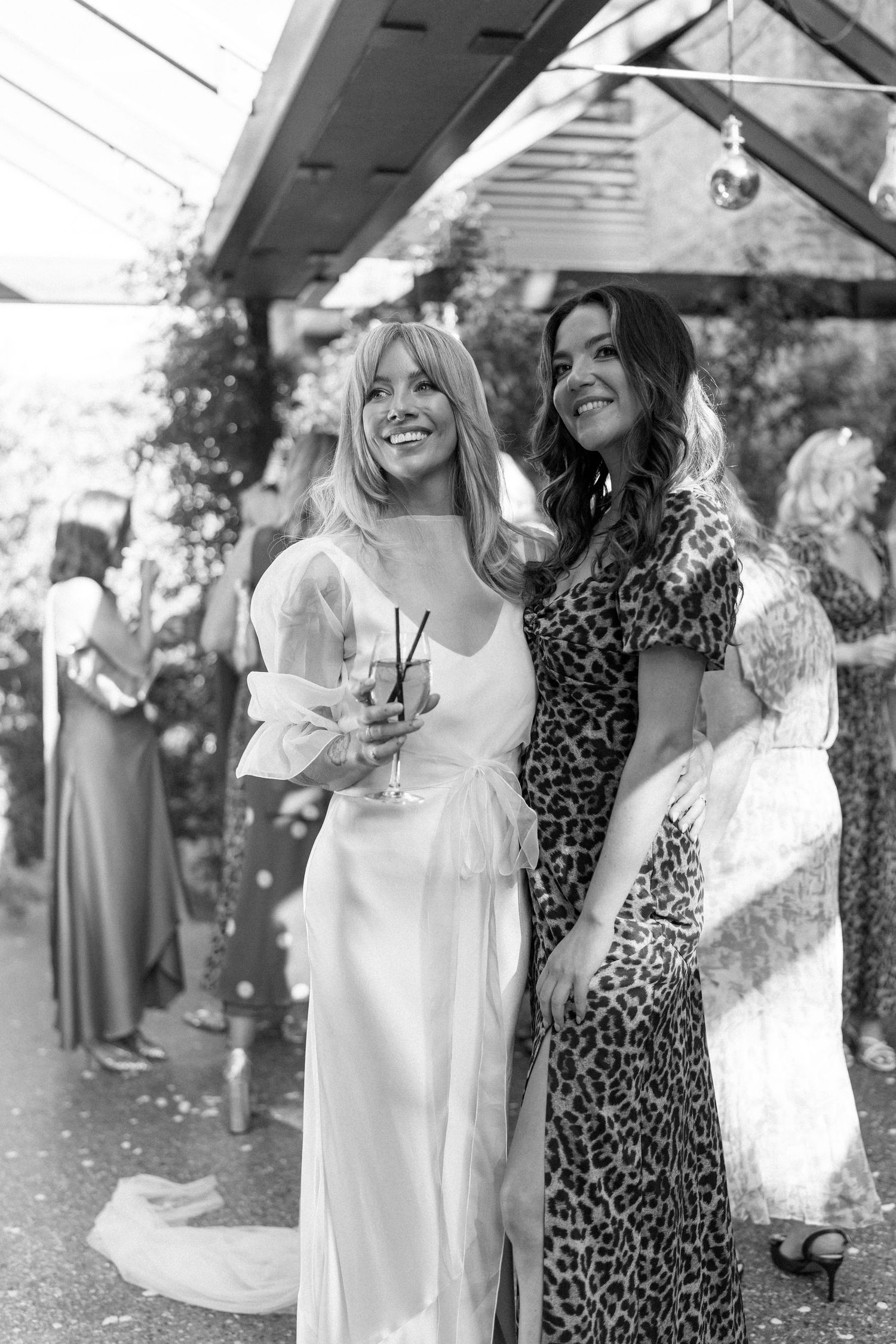 Black and white photo of wedding guests in leopard print and white dresses at outdoor reception.