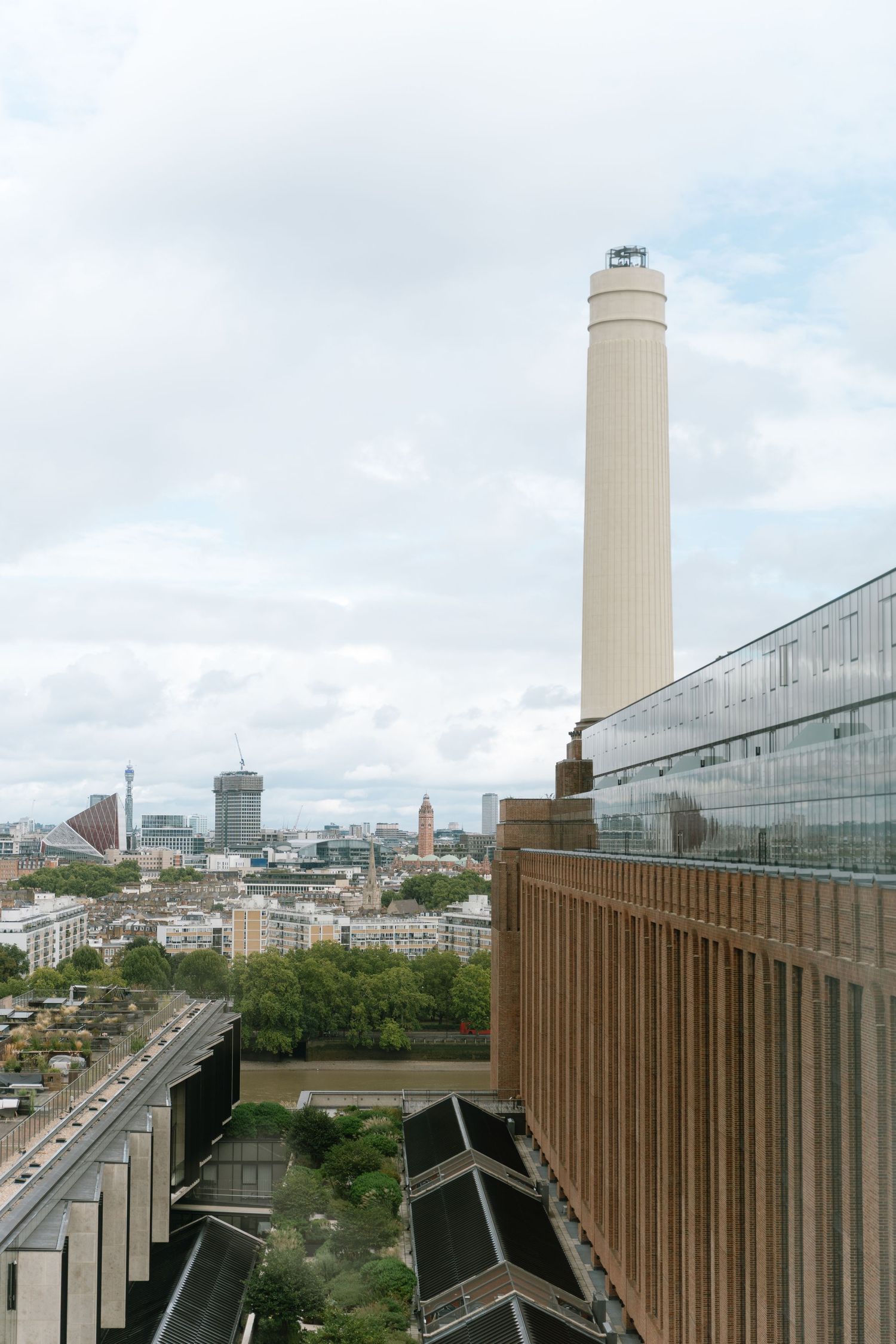 Modern university campus buildings with tall towers and wooden architectural details against a cloudy city skyline.