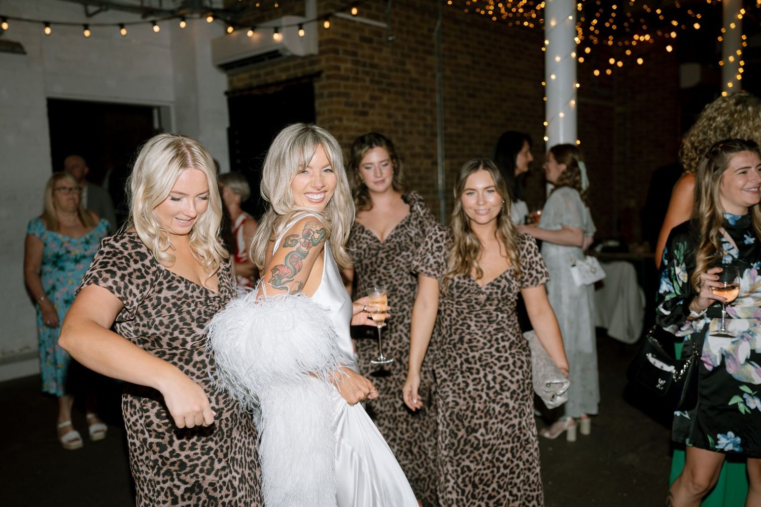 Wedding party in leopard print dresses celebrating on dance floor with bride in white.