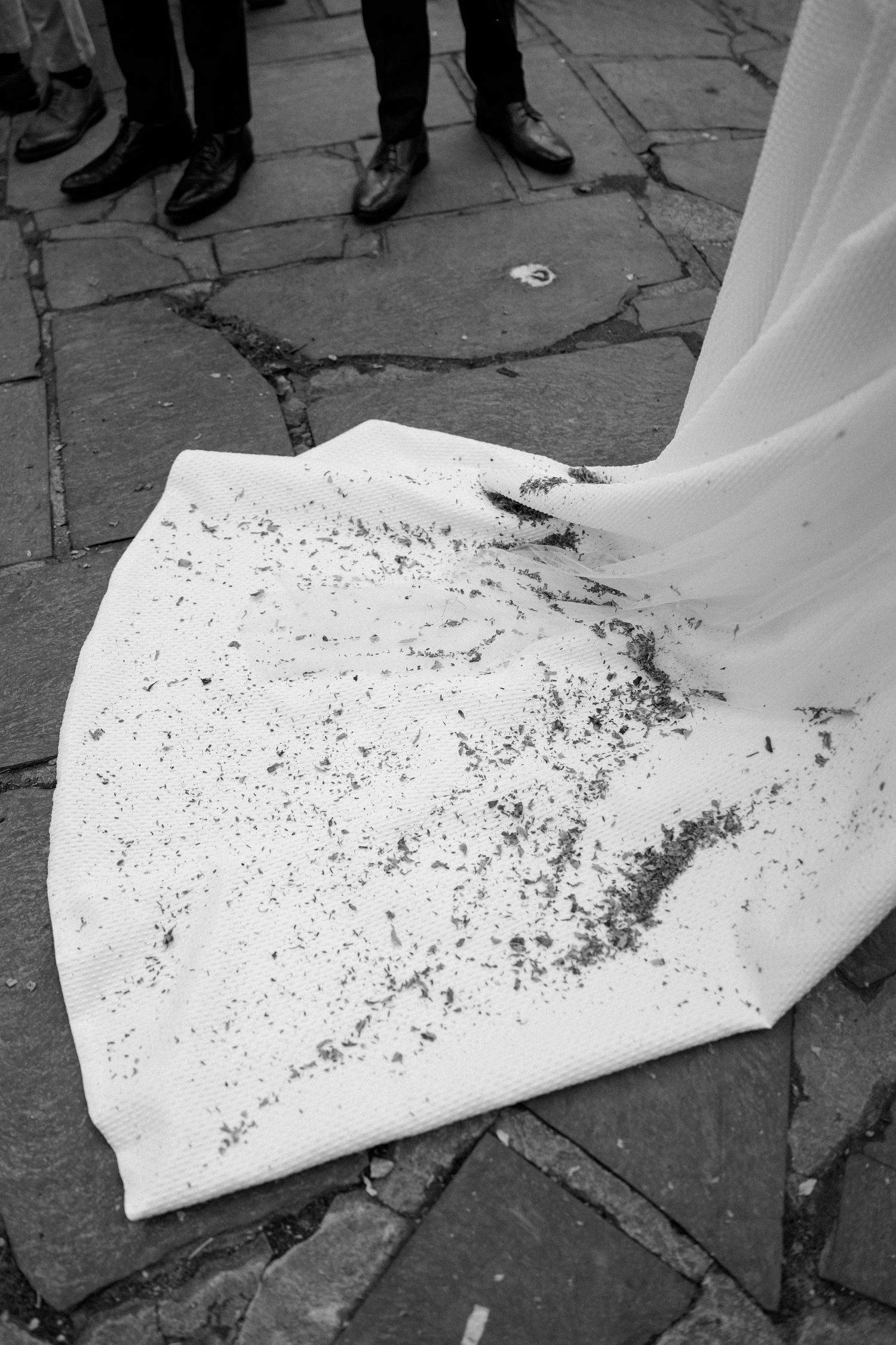 A black and white photo showing the muddy hem of a wedding dress on stone pavement.