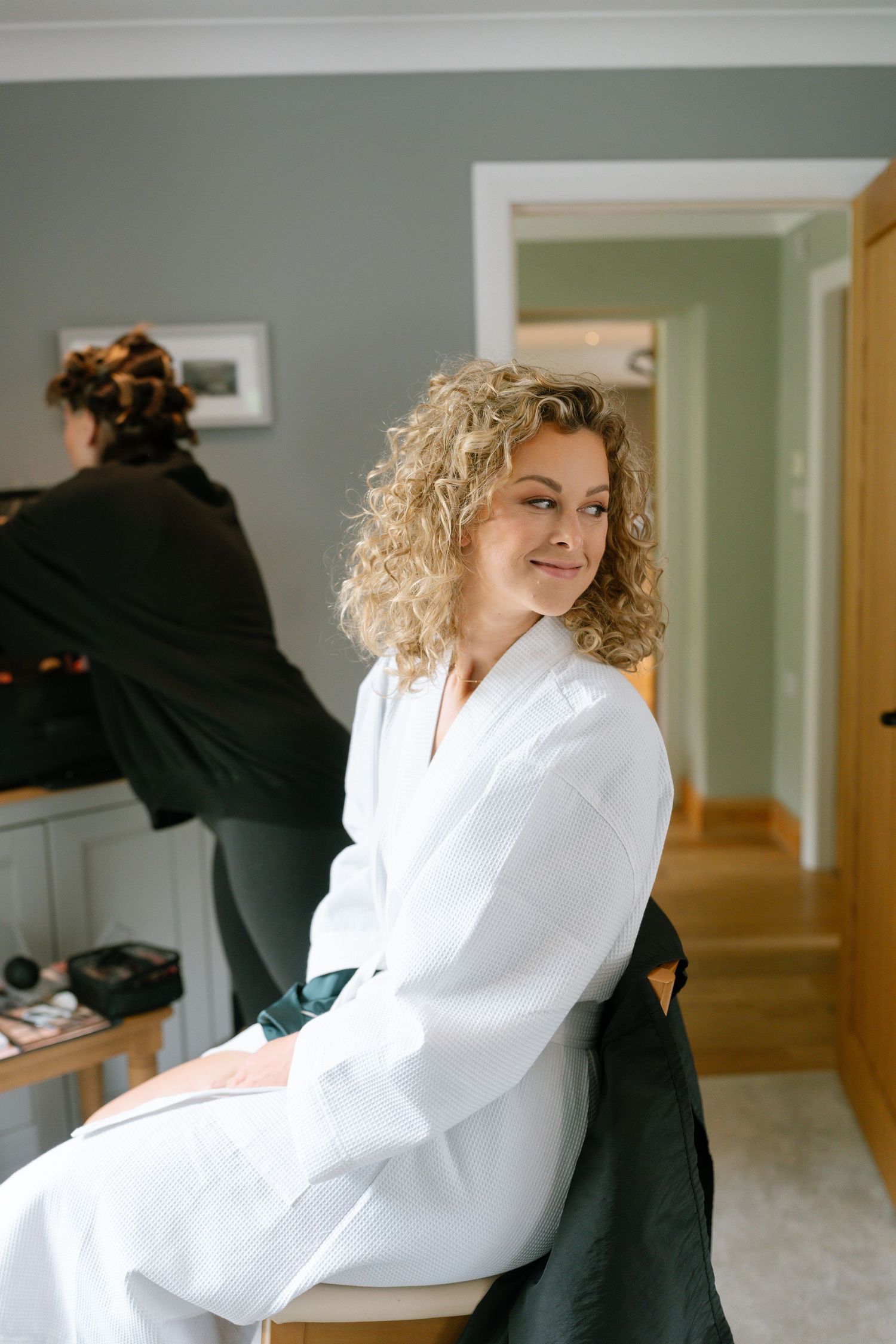 A sequence of candid moments showing someone in a white top and curly hair getting ready in a hallway.