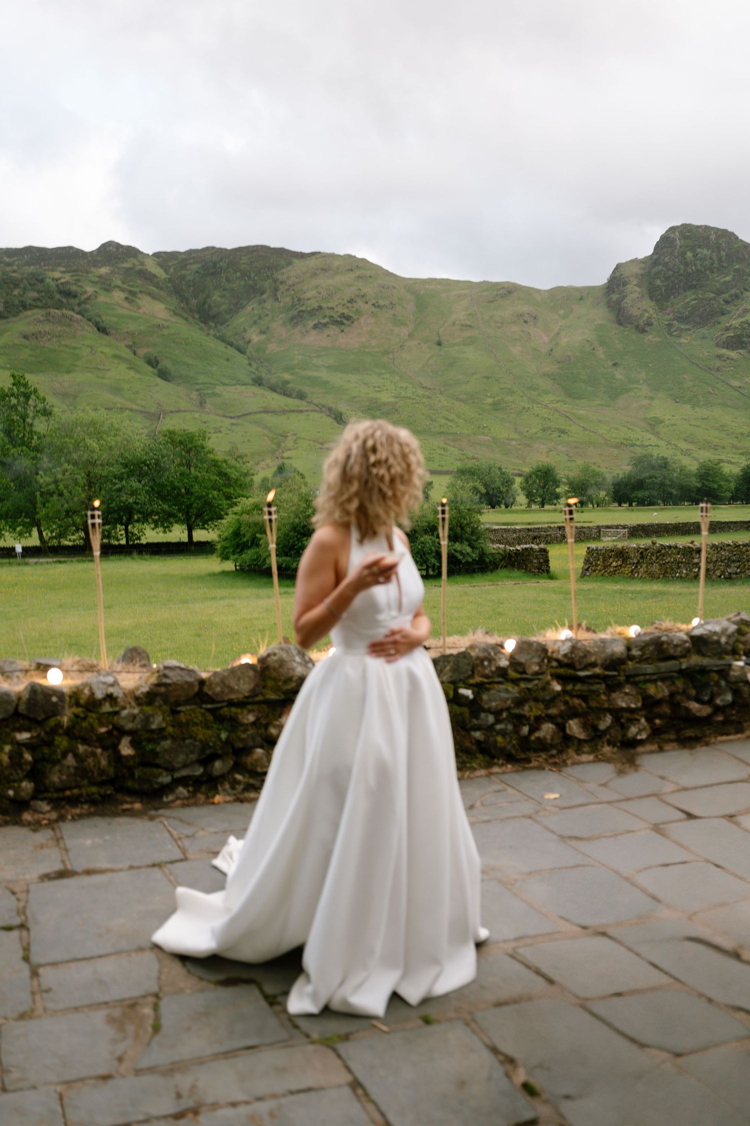 Bride in flowing white dress twirling on stone patio with mountain backdrop.
