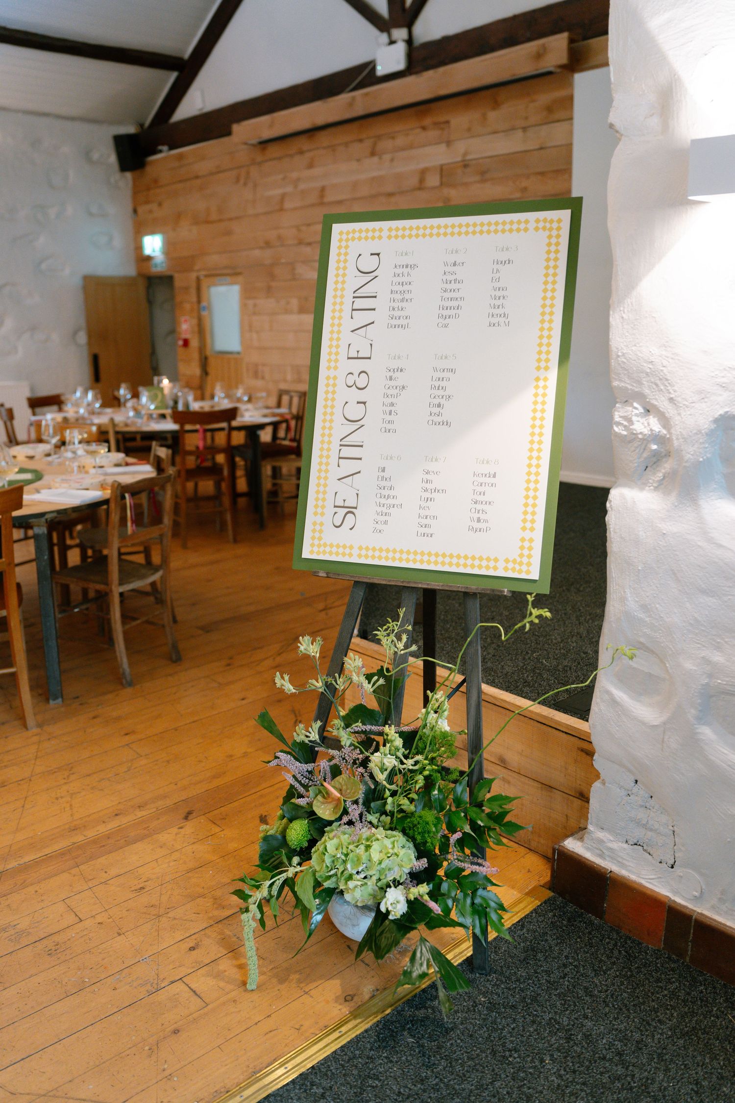 Wedding seating chart display with floral arrangements in a rustic indoor venue.