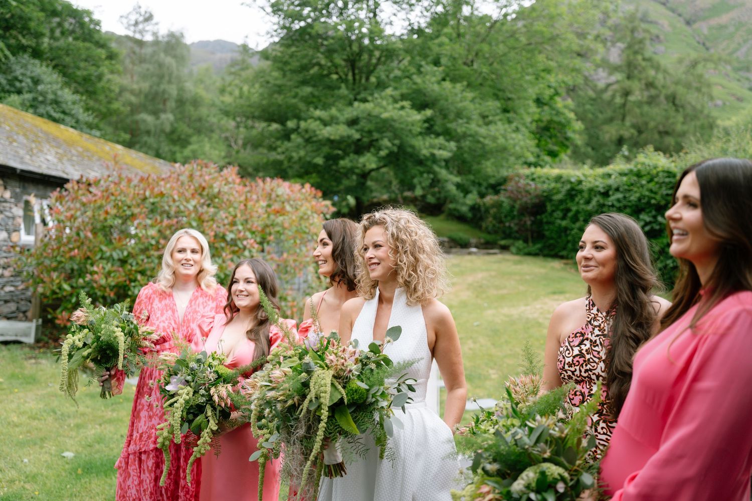 Bridesmaids in pink dresses walking outdoors with floral bouquets.