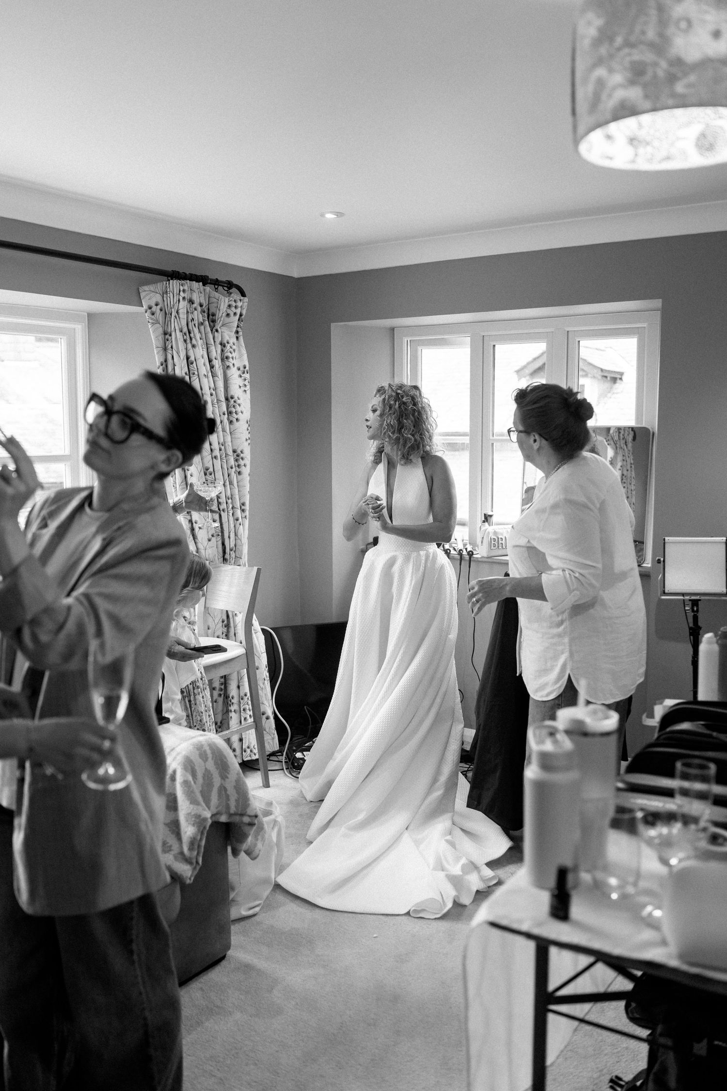 A black and white photo showing wedding preparations in a room with gray walls and floral curtains.
