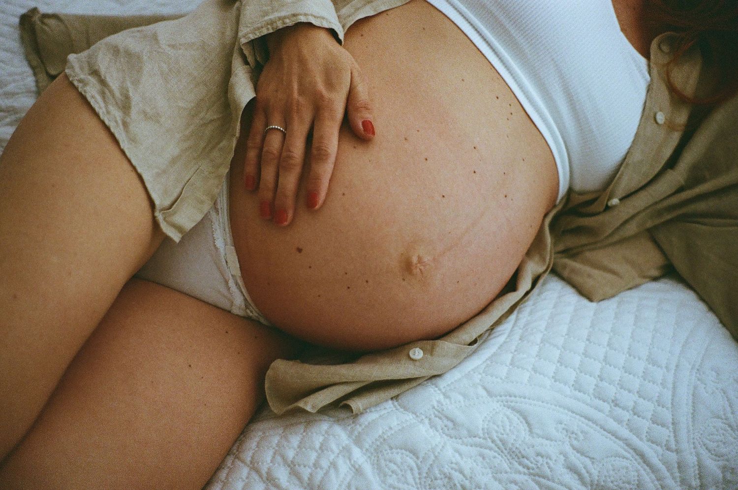 A close-up view of a pregnant belly with a hand resting gently on the bare skin against white bedding.