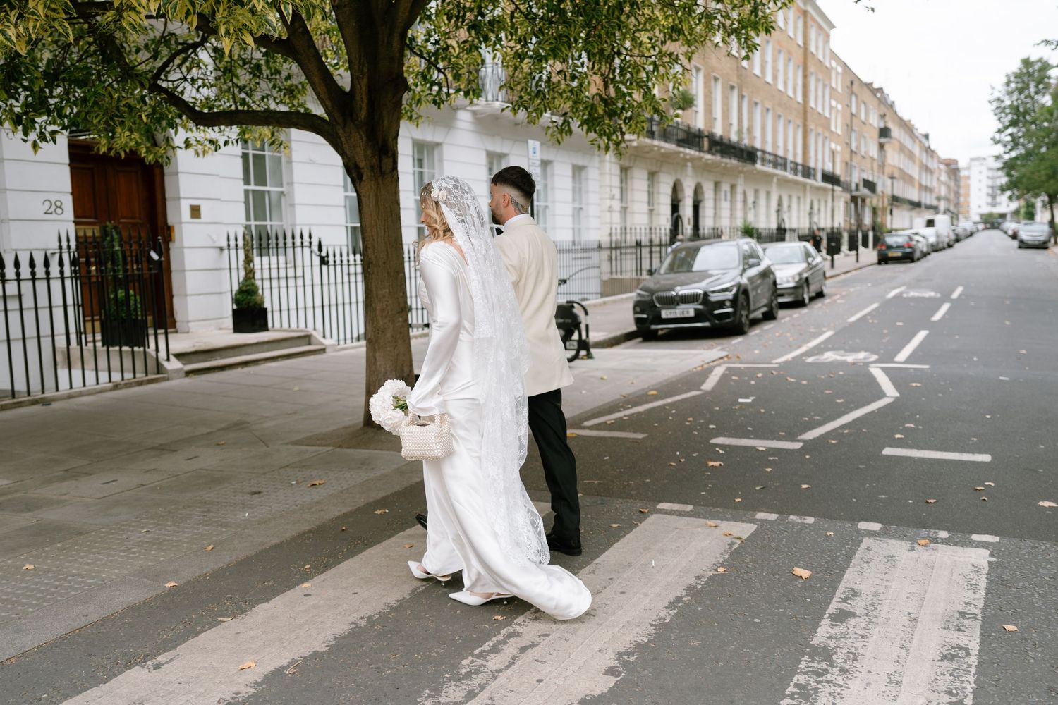Wedding party walks down a tree-lined city street in formal attire.