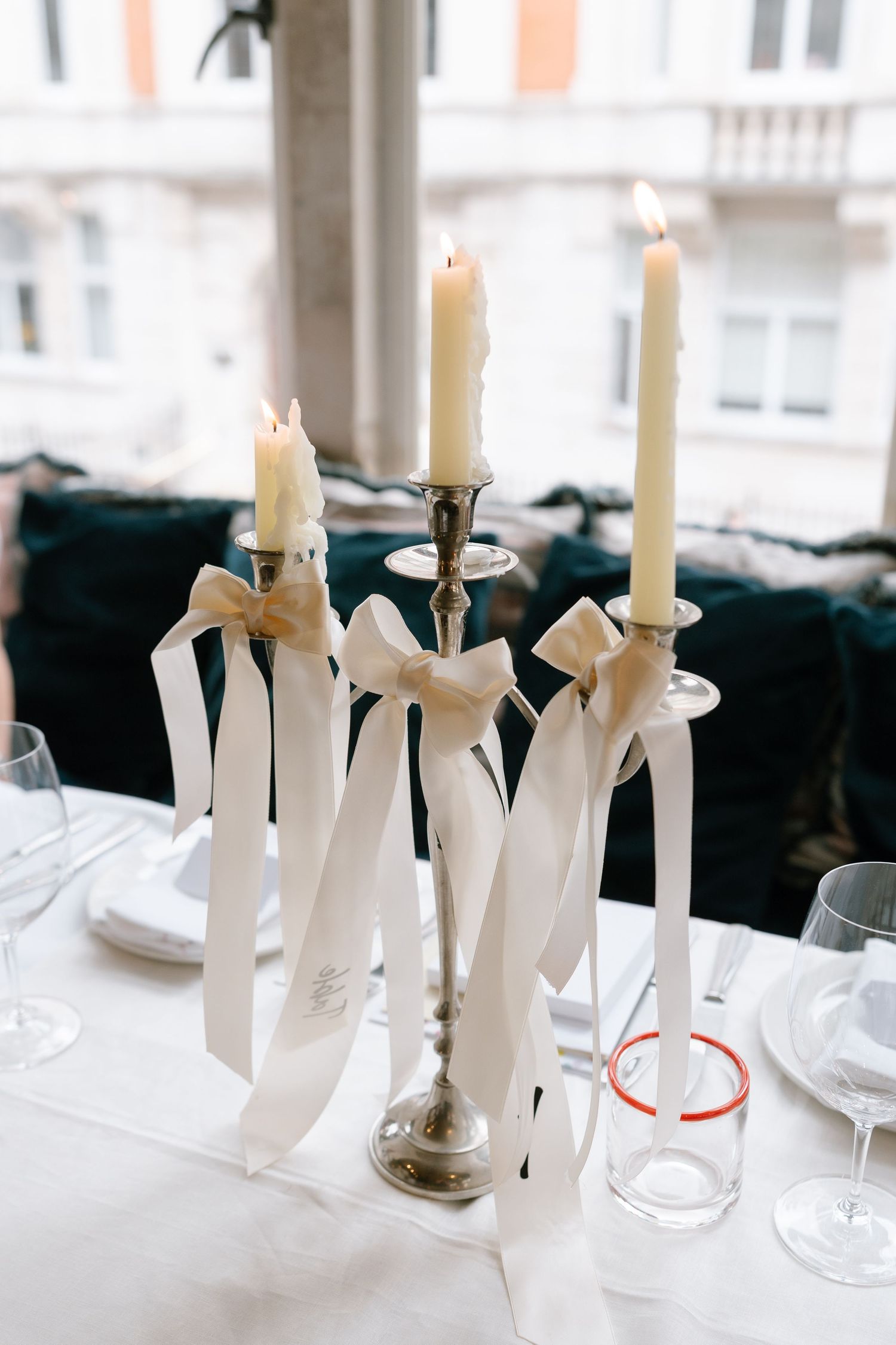 Elegant table setting with white taper candles tied with ribbon in silver holders.