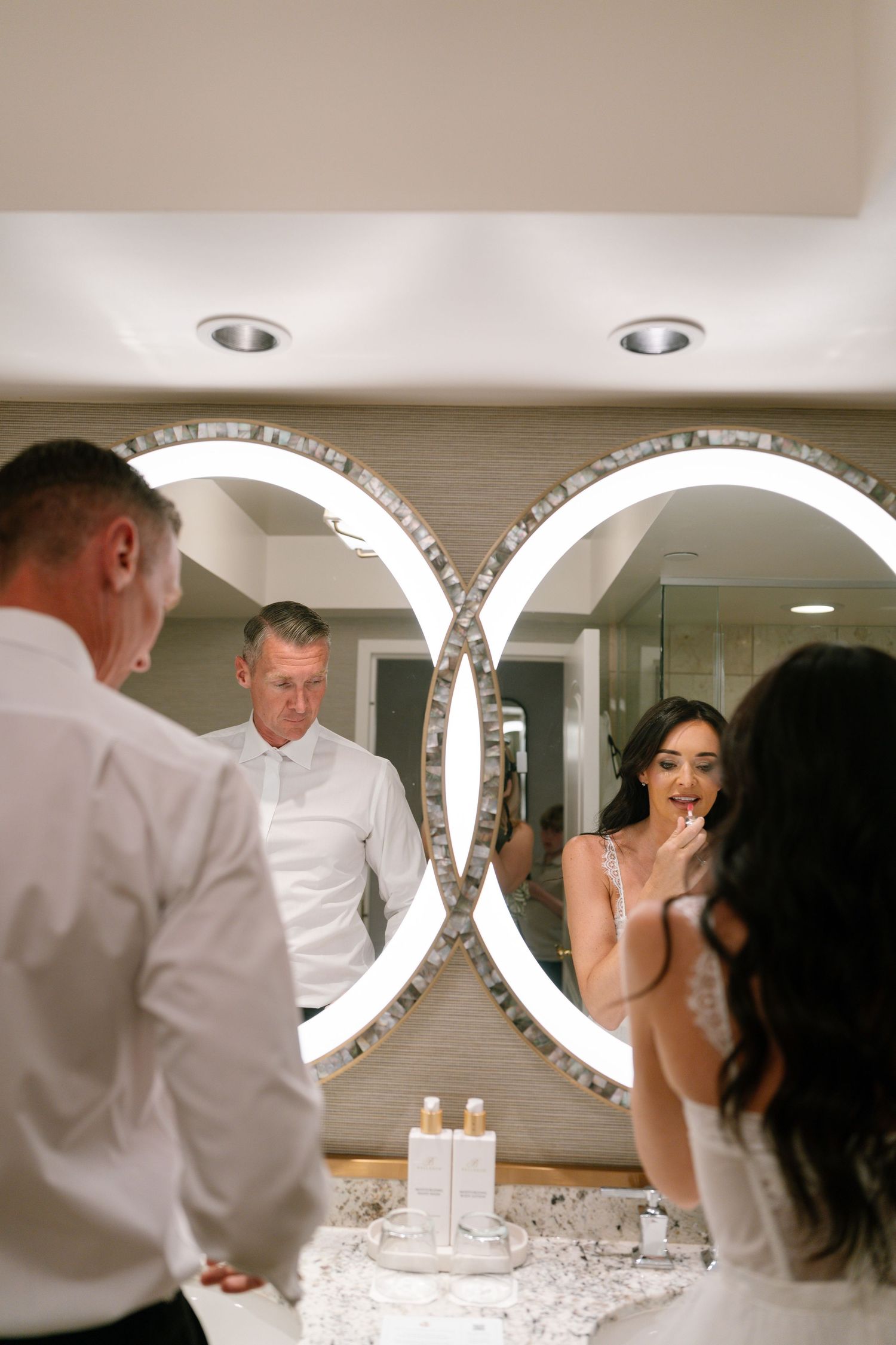 Wedding couple looking in illuminated circular mirrors during preparation.