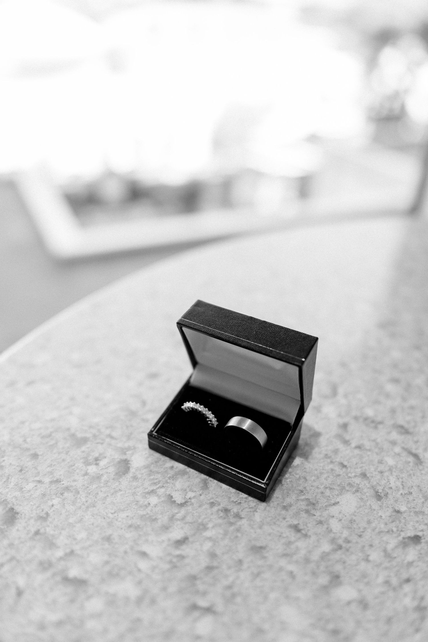 Wedding rings displayed in an open black jewelry box on a stone surface.