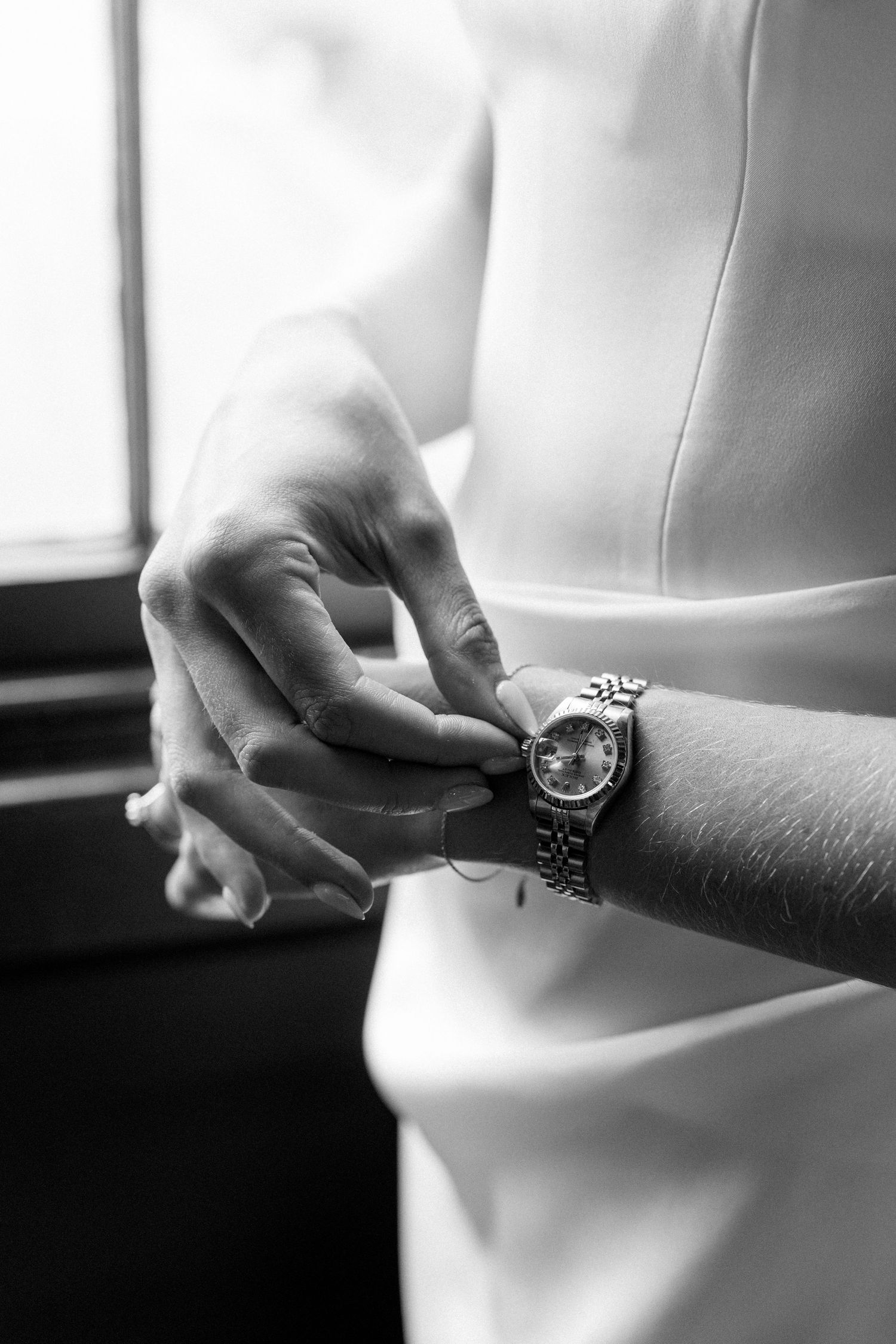 Close-up of bride in white dress fastening a silver Rolex watch on her wrist before the ceremony.