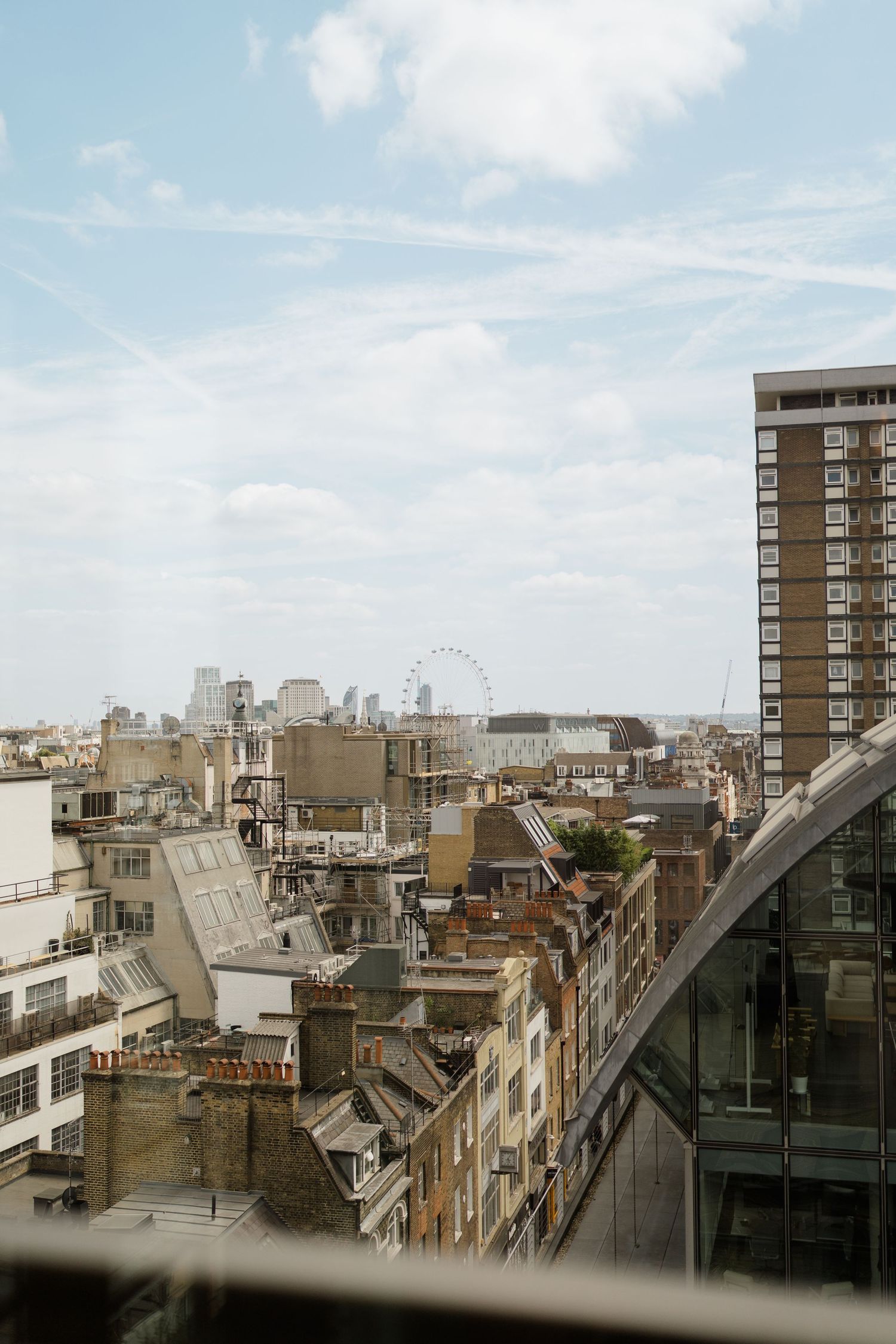 Aerial view of London rooftops with the London Eye ferris wheel visible against a partly cloudy sky.