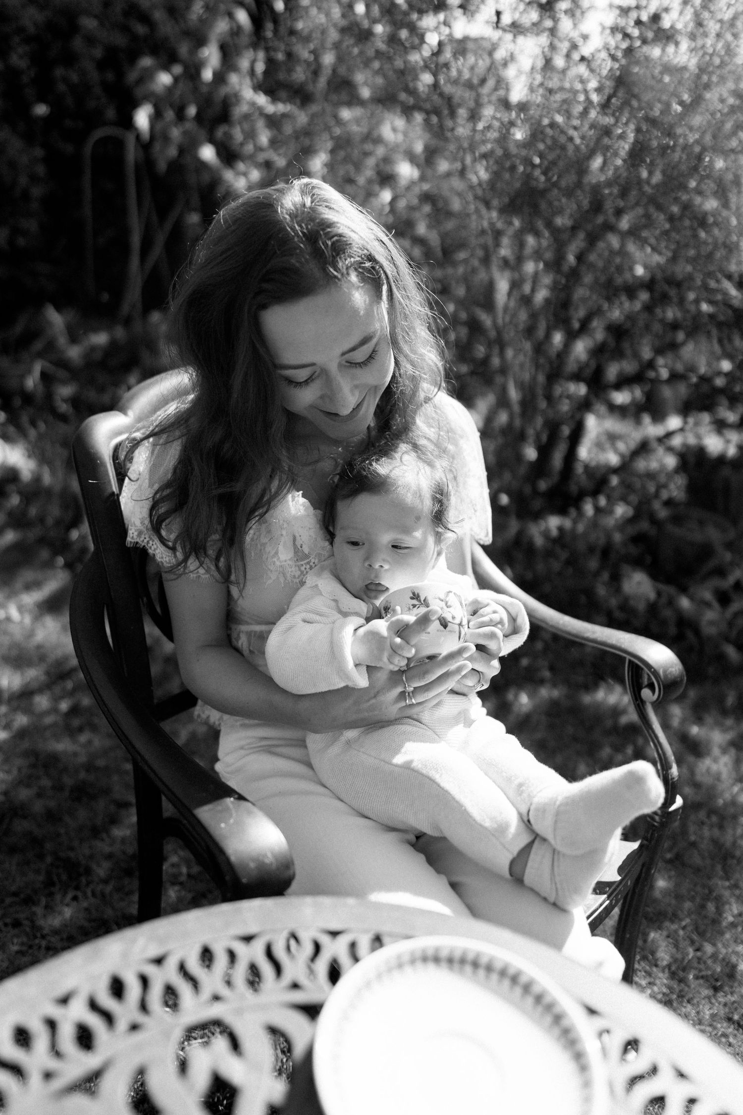 Tender moment between mother and baby sitting in white garden chair.