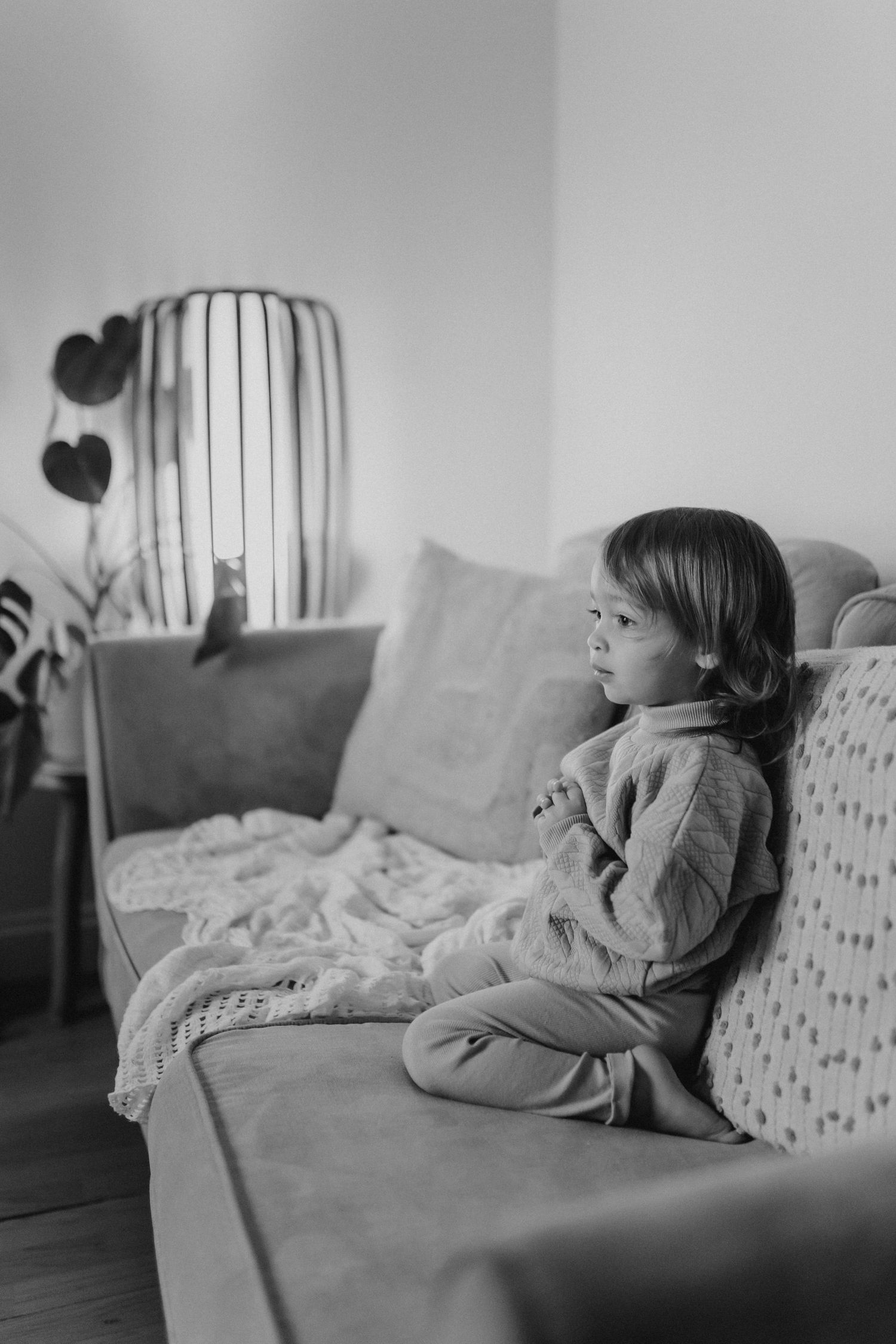 A child relaxes on a grey couch with patterned pillows in natural light.