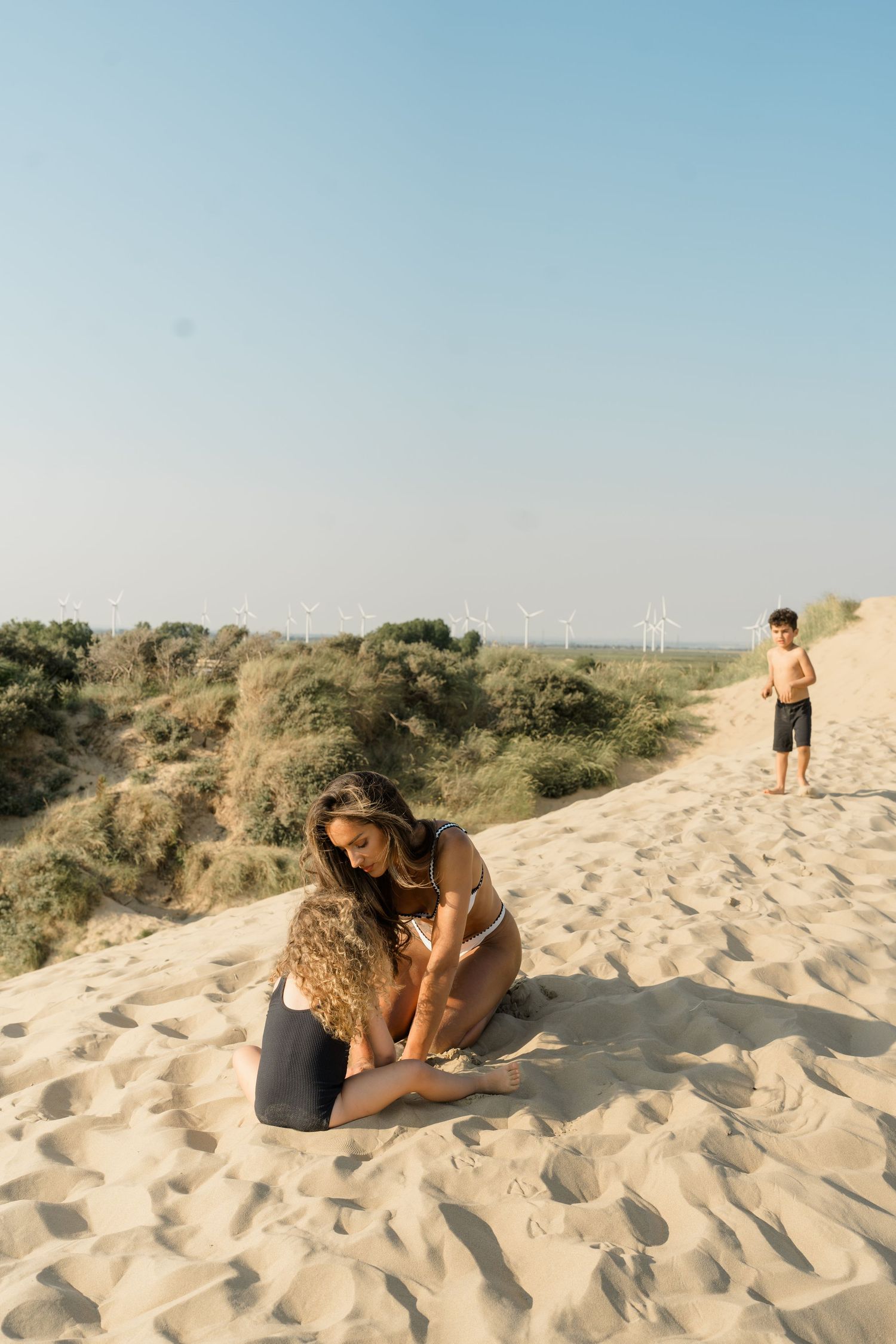 People enjoying a sunny day on sand dunes with coastal vegetation.