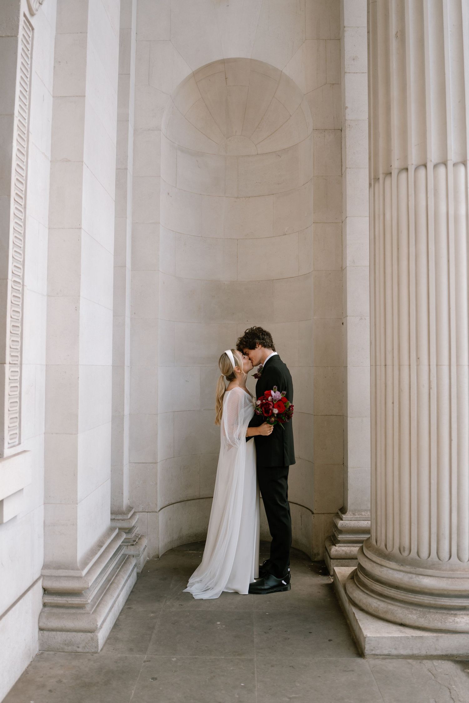 Intimate moment between newlyweds in alcove between classical columns.