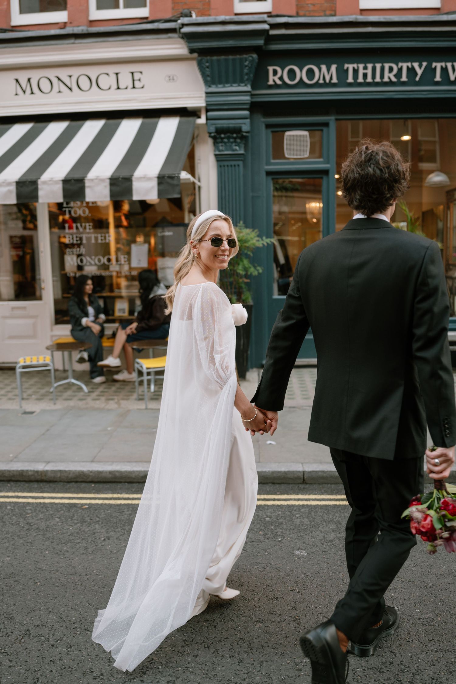 Wedding couple walking hand in hand past urban storefronts with striped awnings.