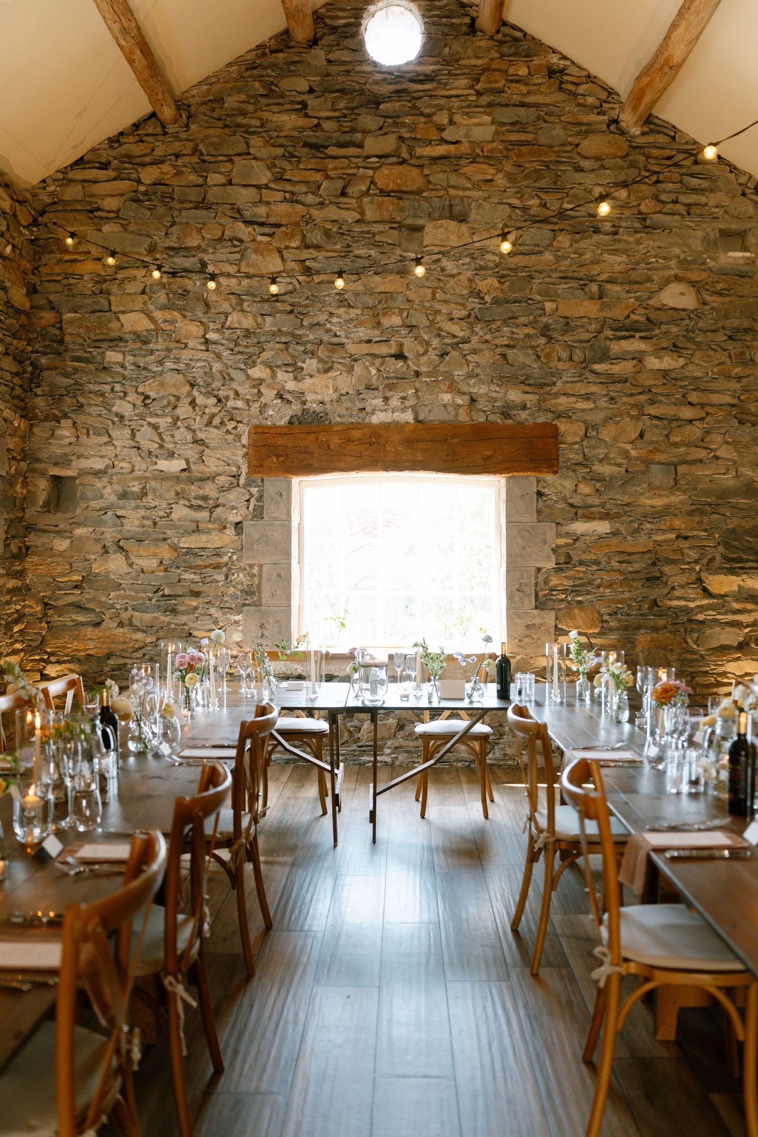 Rustic stone barn venue with wooden tables set for wedding reception under string lights.