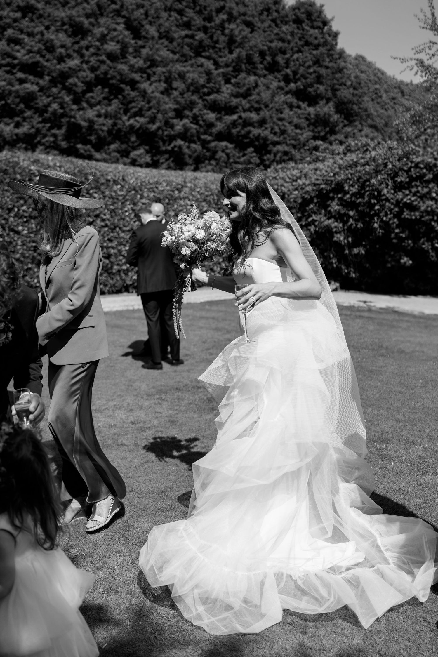 A bride in a flowing white gown stands in a garden setting during the wedding reception.
