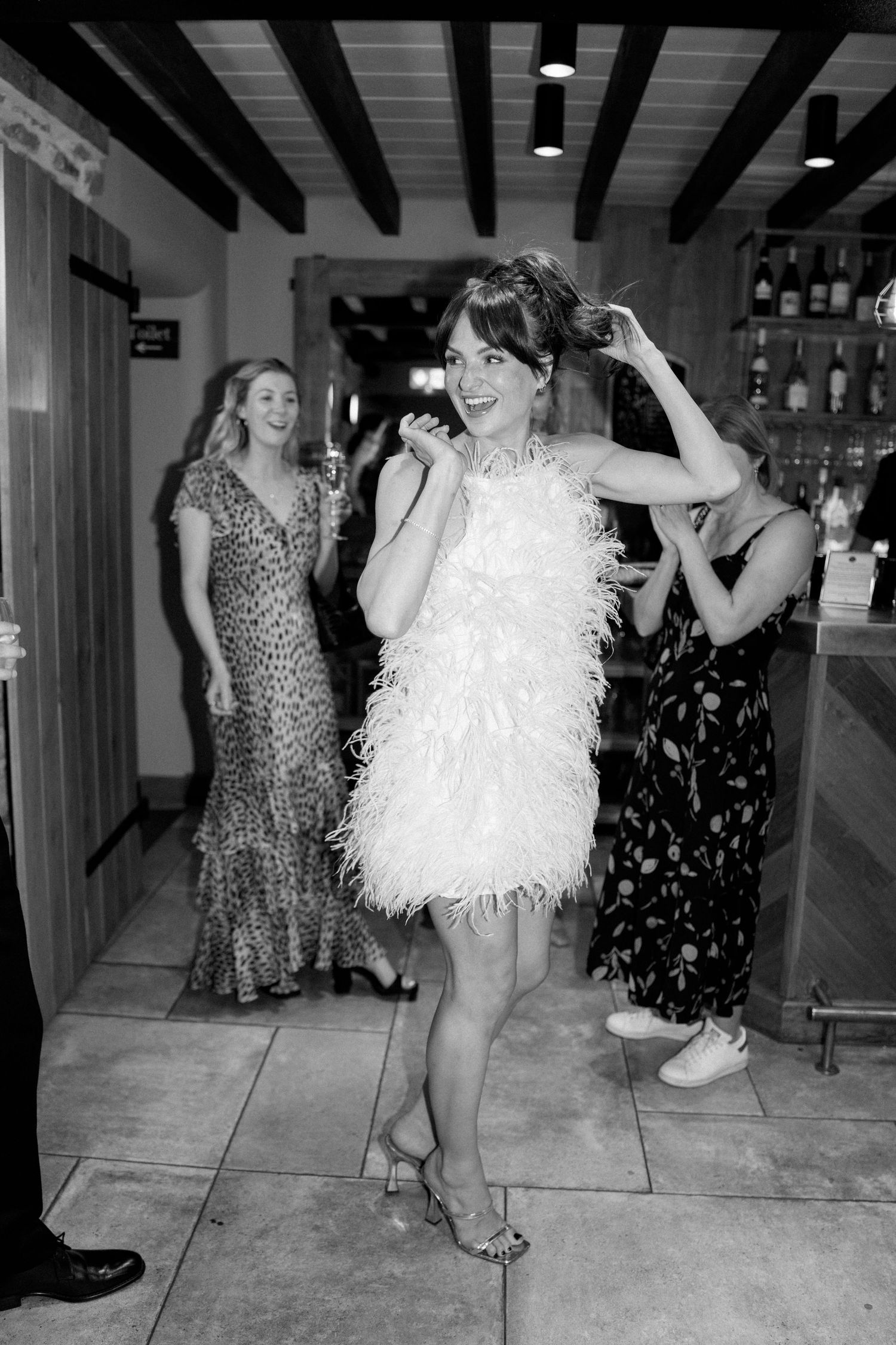 Party scene with people dancing, featuring a white feathered dress against rustic wooden beams.