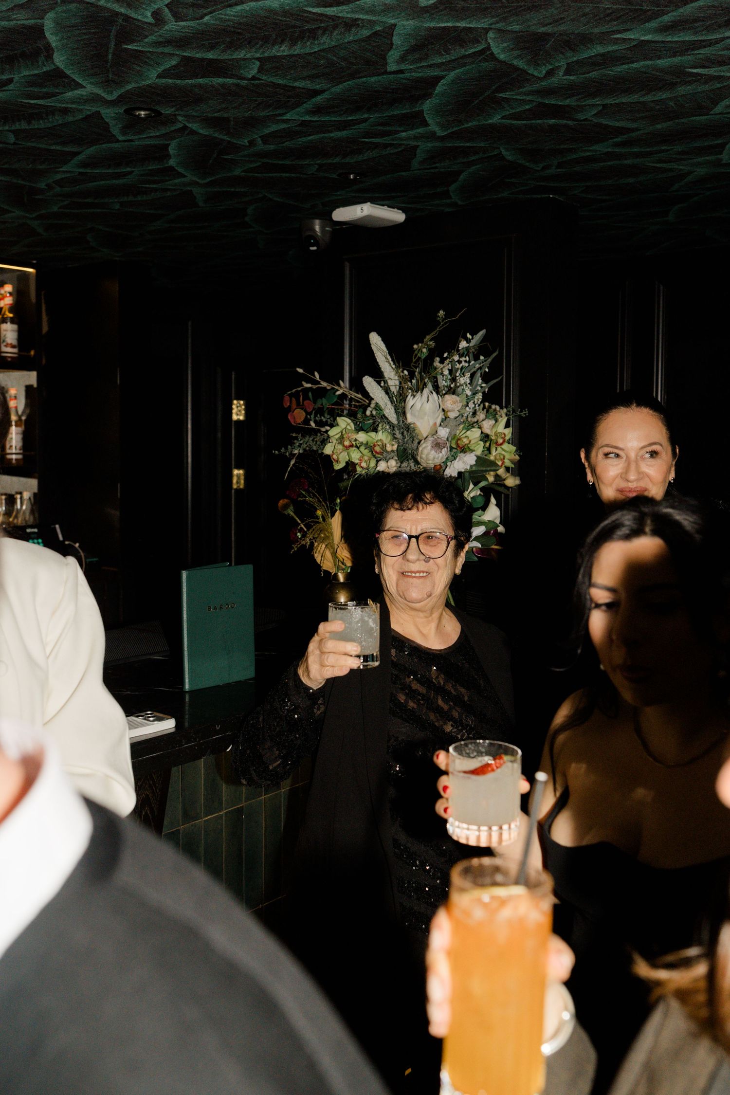Elderly woman smiling and raising a cocktail glass at an elegant wedding reception.