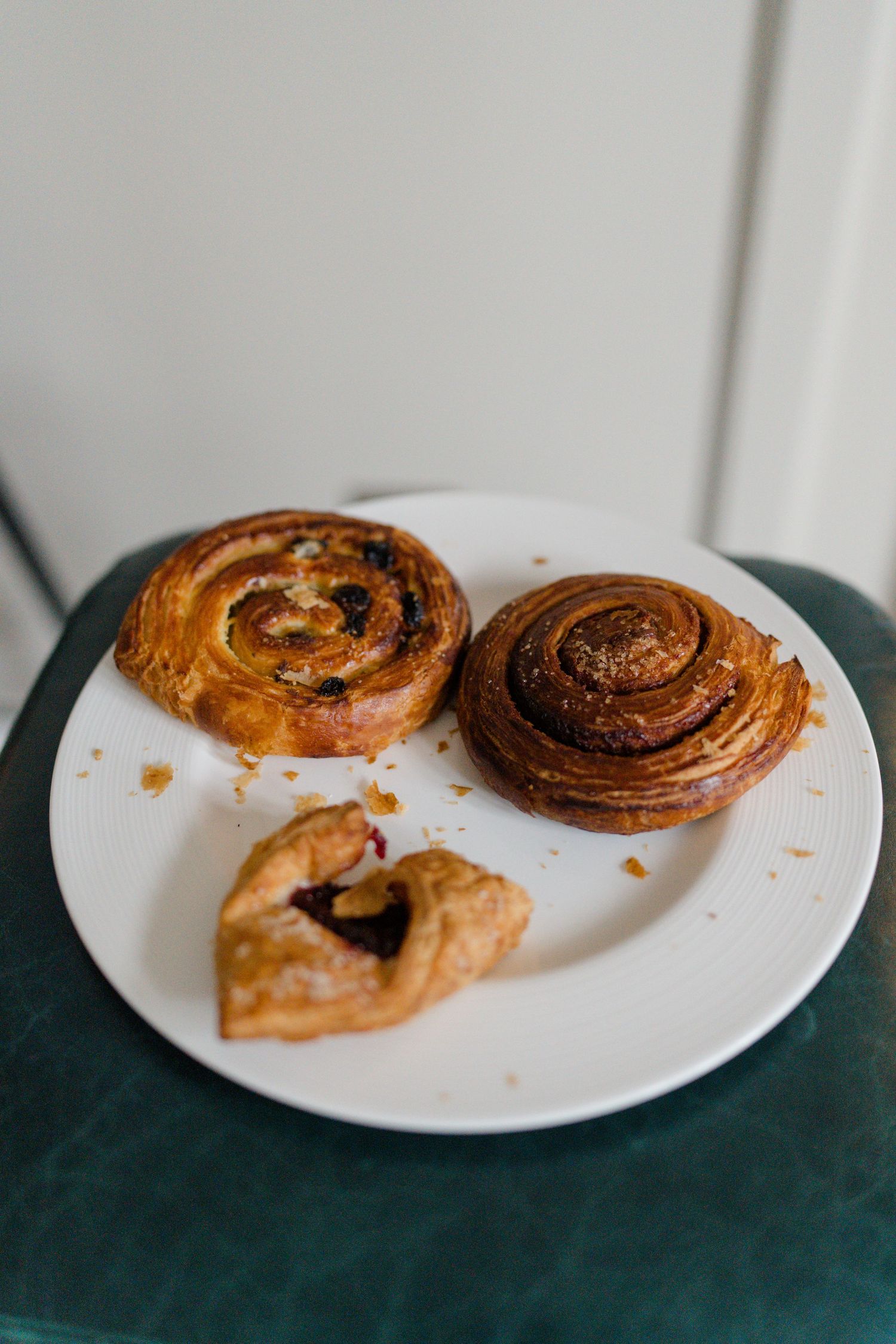 Three assorted pastries including two spiral Danish rolls and a jam-filled pastry on a white plate.