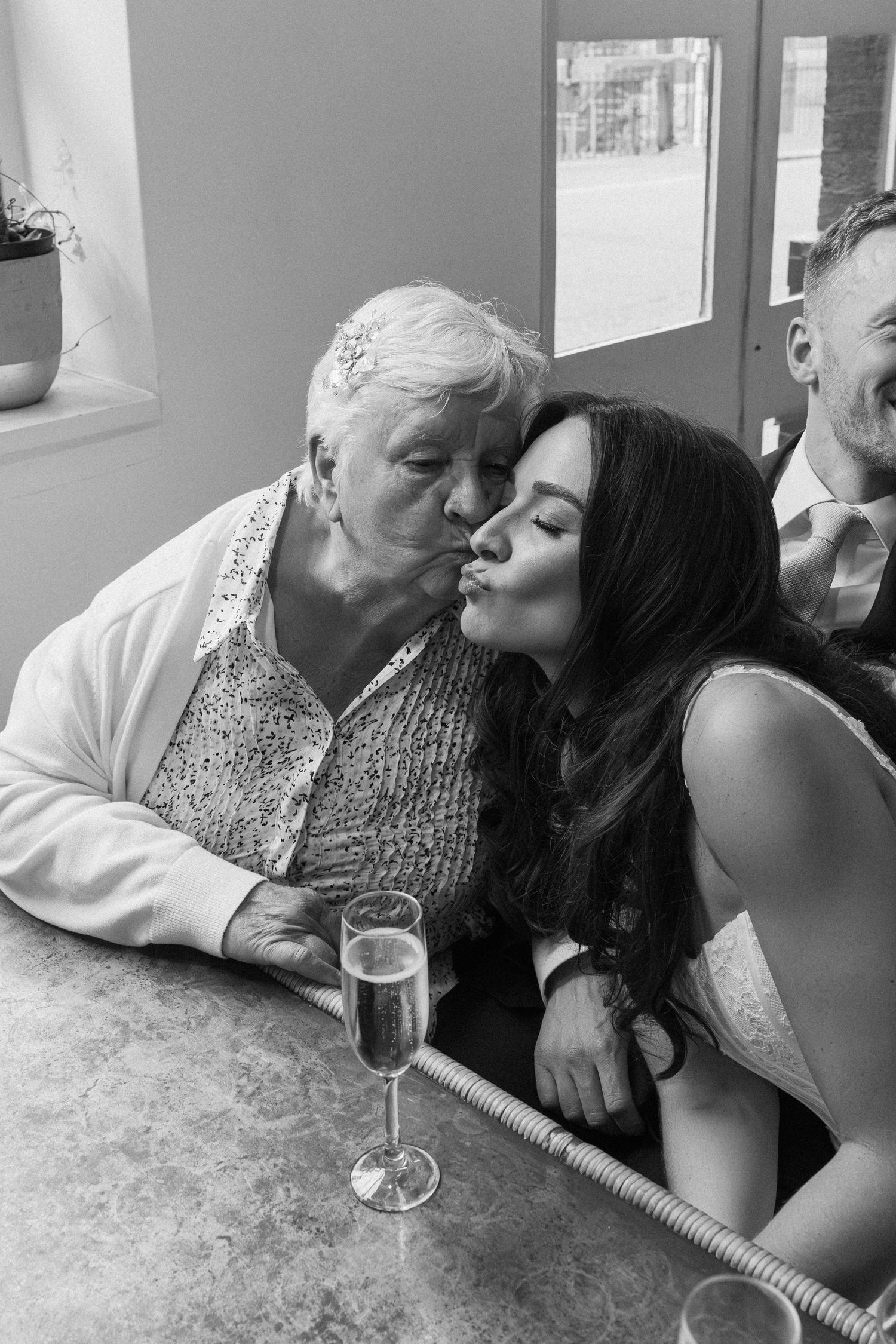 Bride in wedding dress sharing a kiss on the cheek with elderly grandmother at reception.