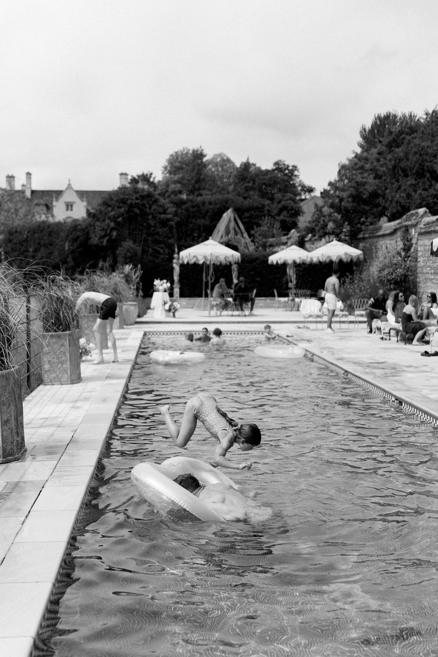 Black and white photo of wedding guest jumping into outdoor pool with inflatable ring at venue.