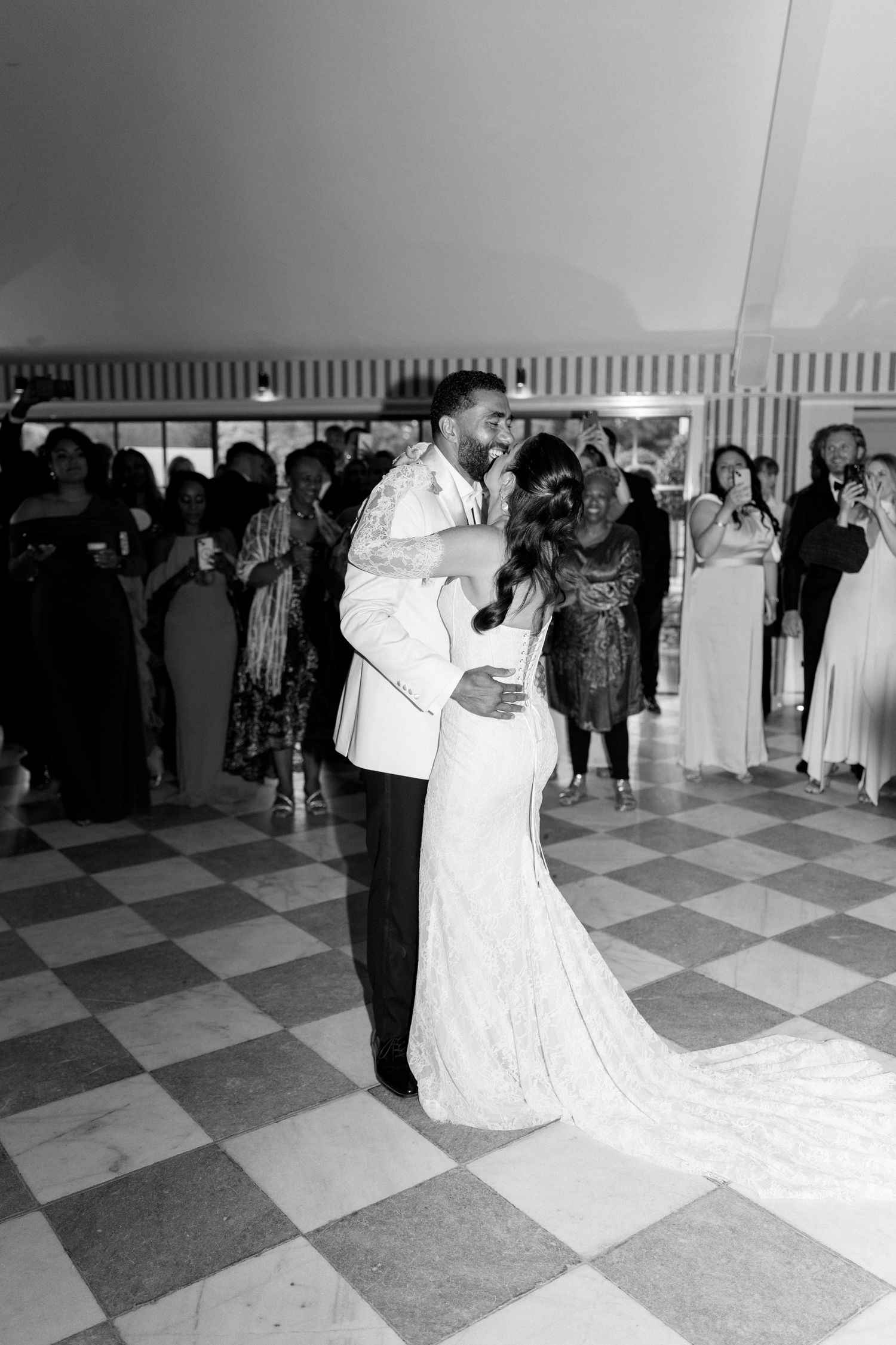 Bride and groom share romantic first dance on checkered floor at wedding reception.