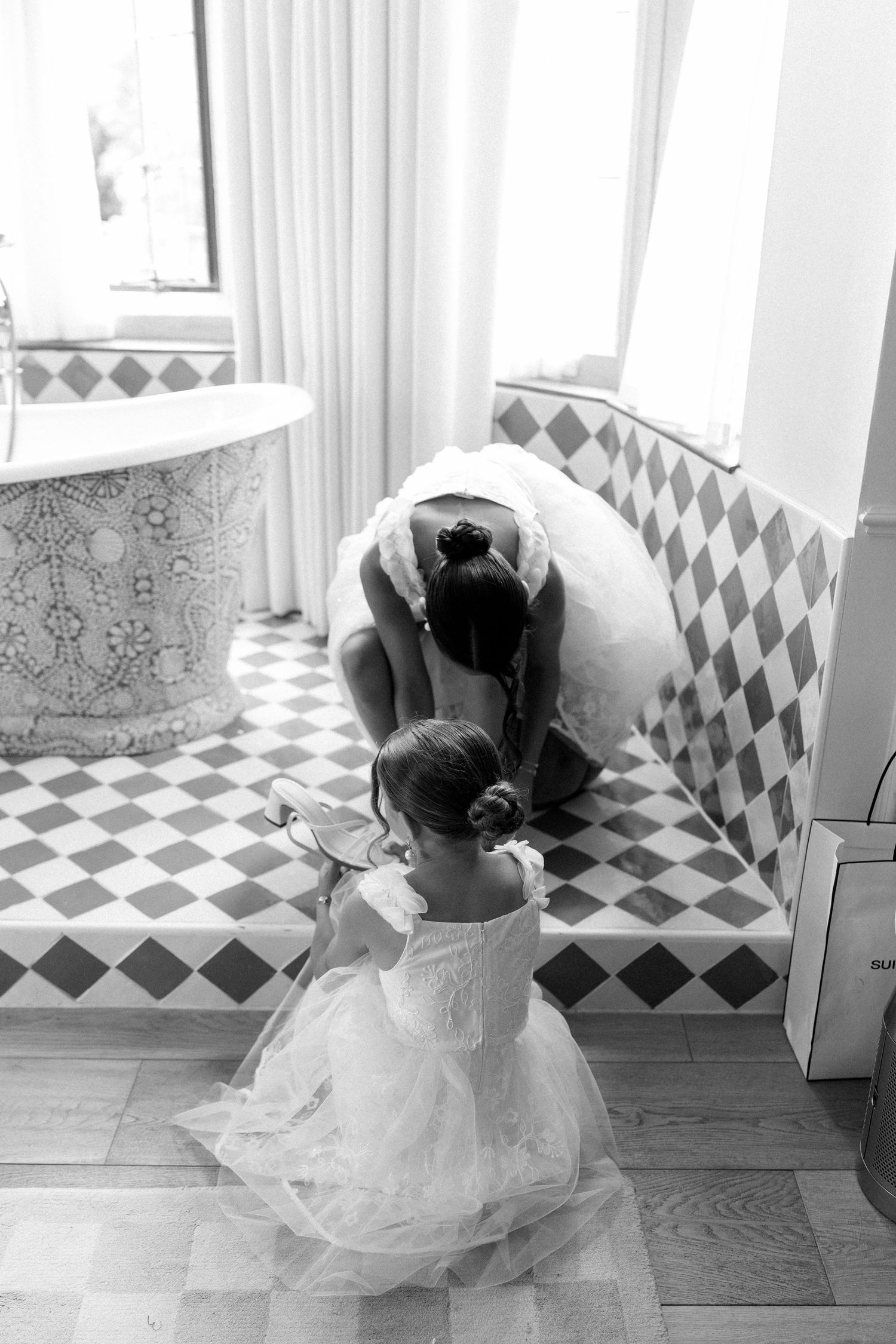 Bride and flower girl sharing a tender moment in a diamond-tiled bathroom.