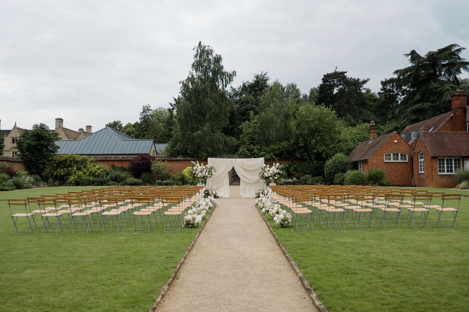Outdoor wedding ceremony setup with white floral arch and rows of chairs on manicured lawn.