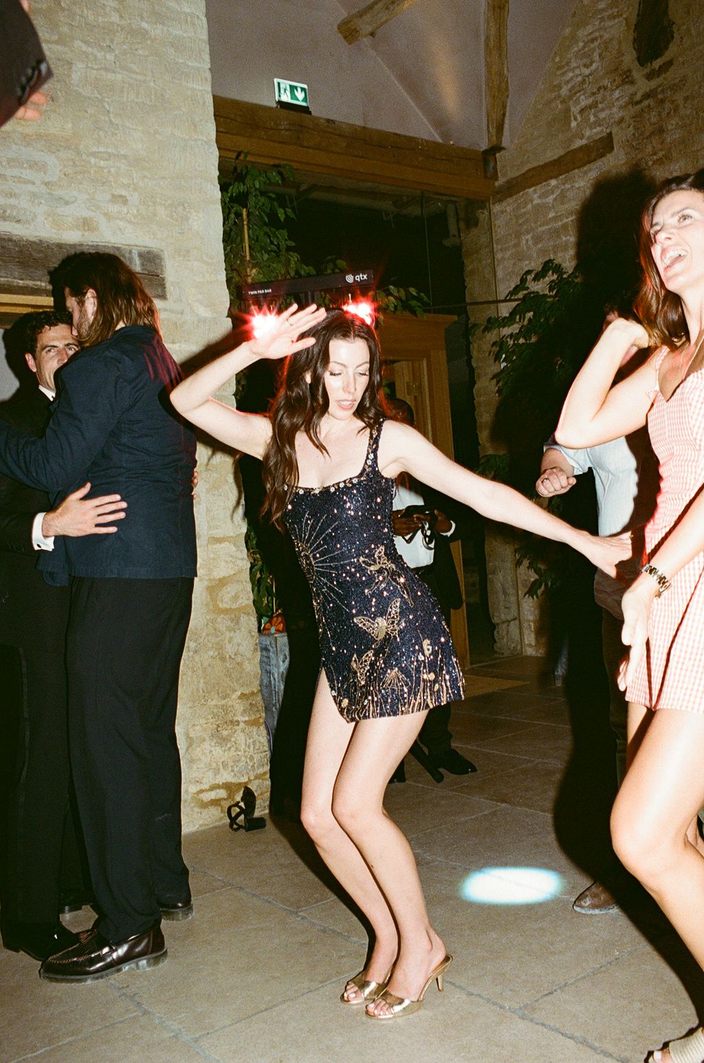 Woman in sequined mini dress dancing energetically at an indoor party with stone walls.