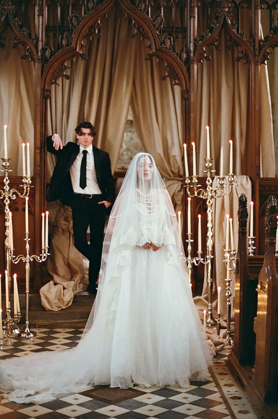 Elegant wedding ceremony in a grand hall with checkered floors and golden candelabras creating a romantic atmosphere.