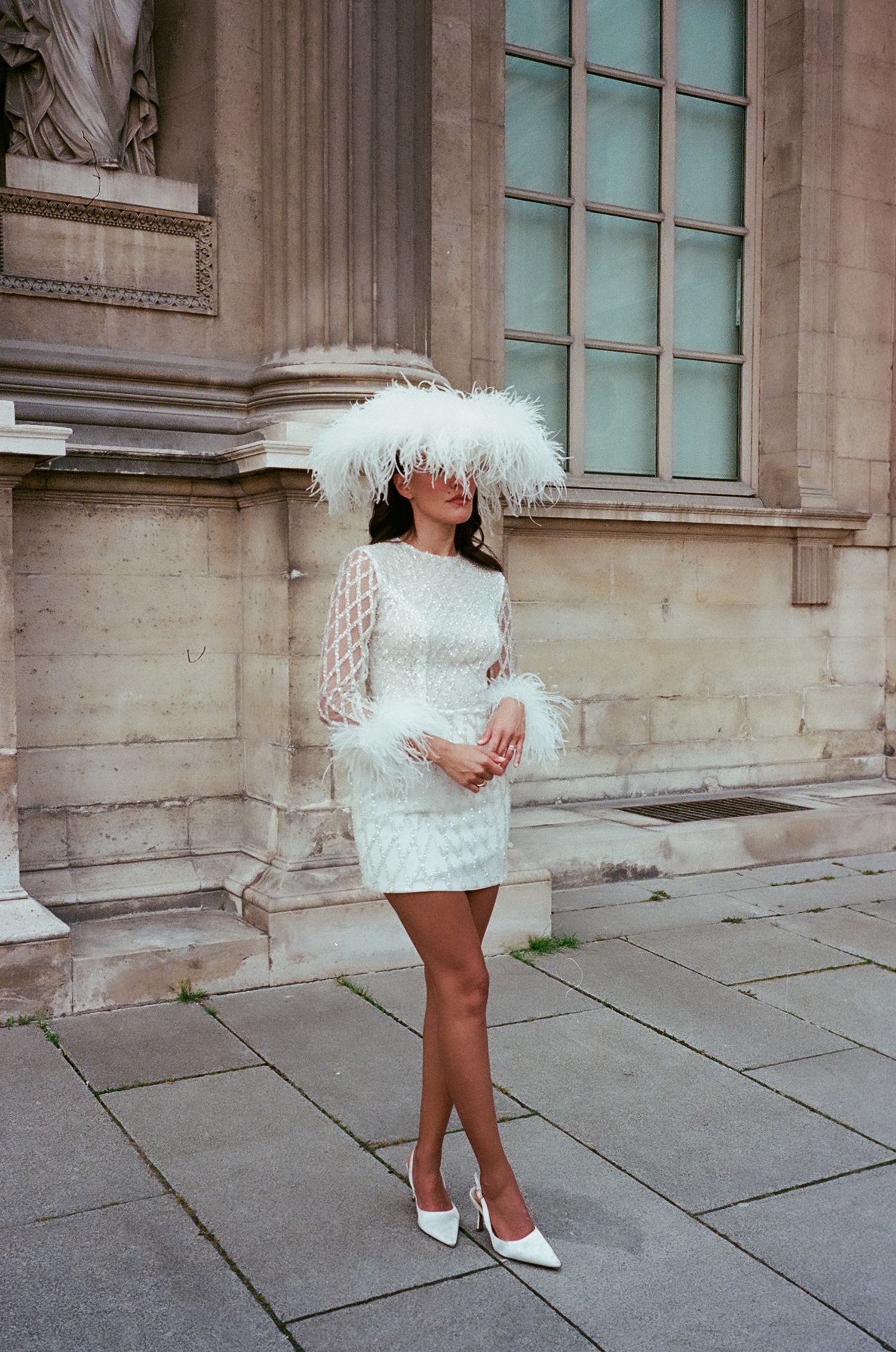 A series of fashion shots showing a white feathered mini dress against a stone building exterior.